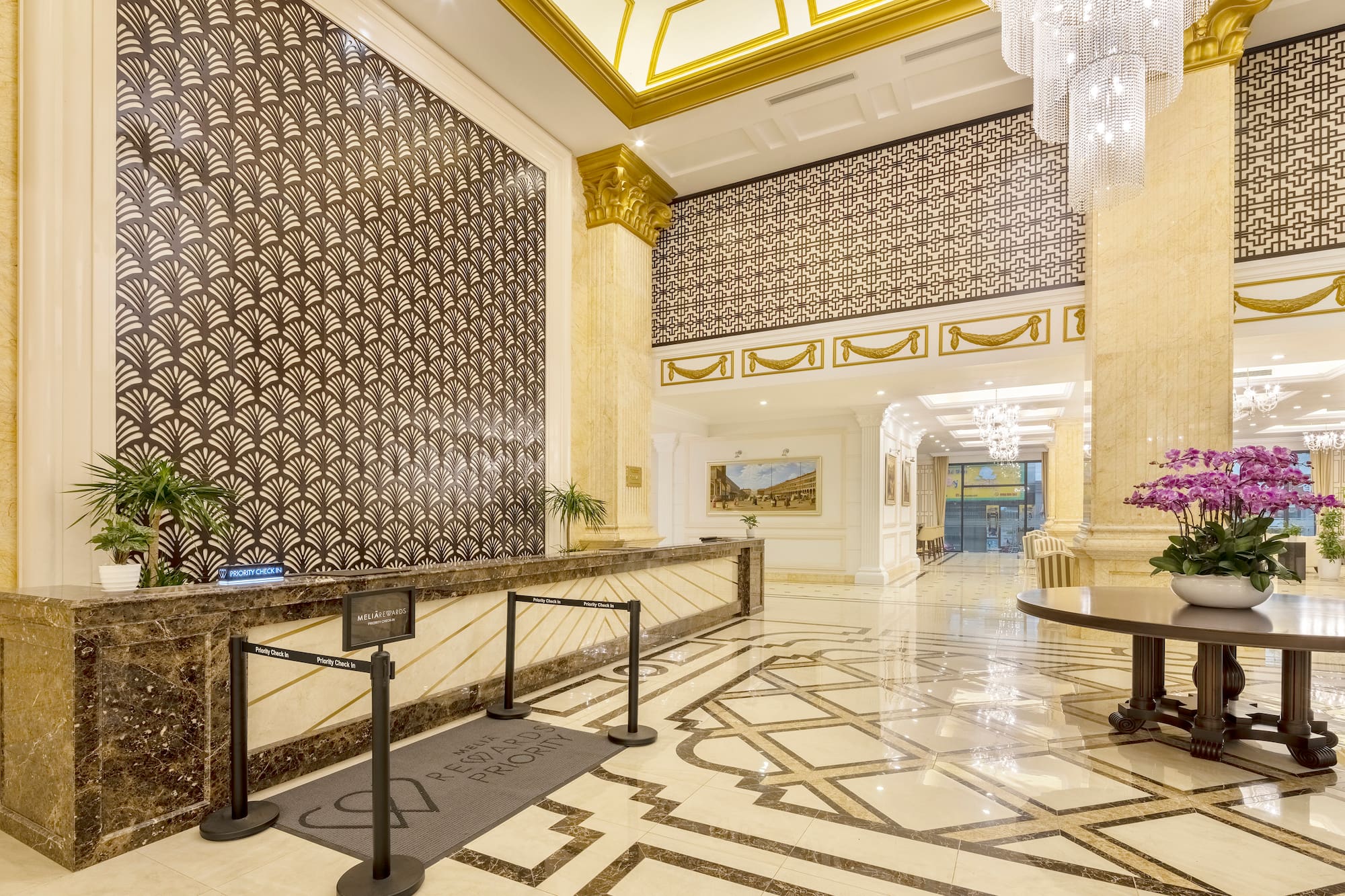 Opulent hotel lobby with marble check-in, gold accents, and grand chandelier.