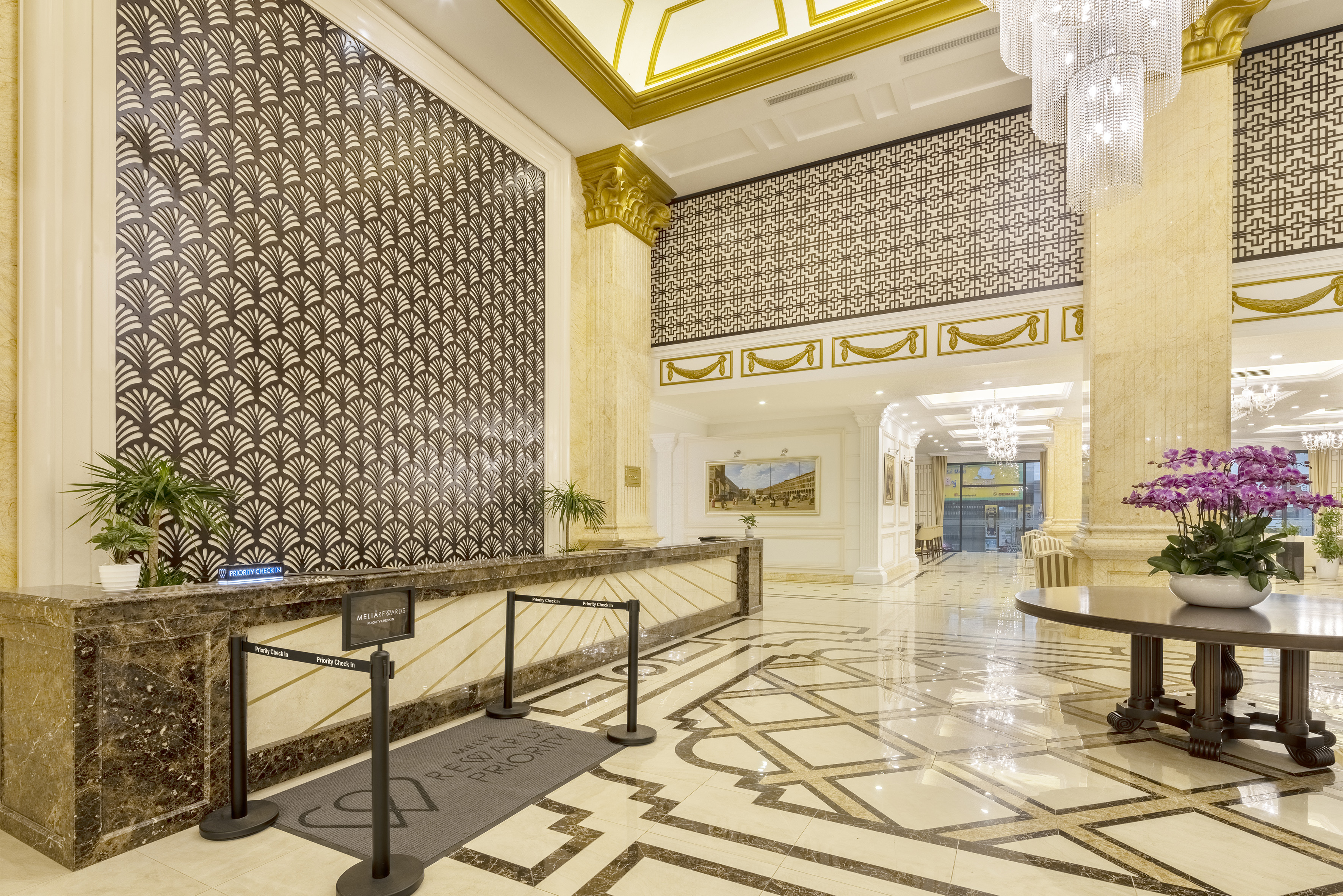 Opulent hotel lobby with marble check-in, gold accents, and grand chandelier.