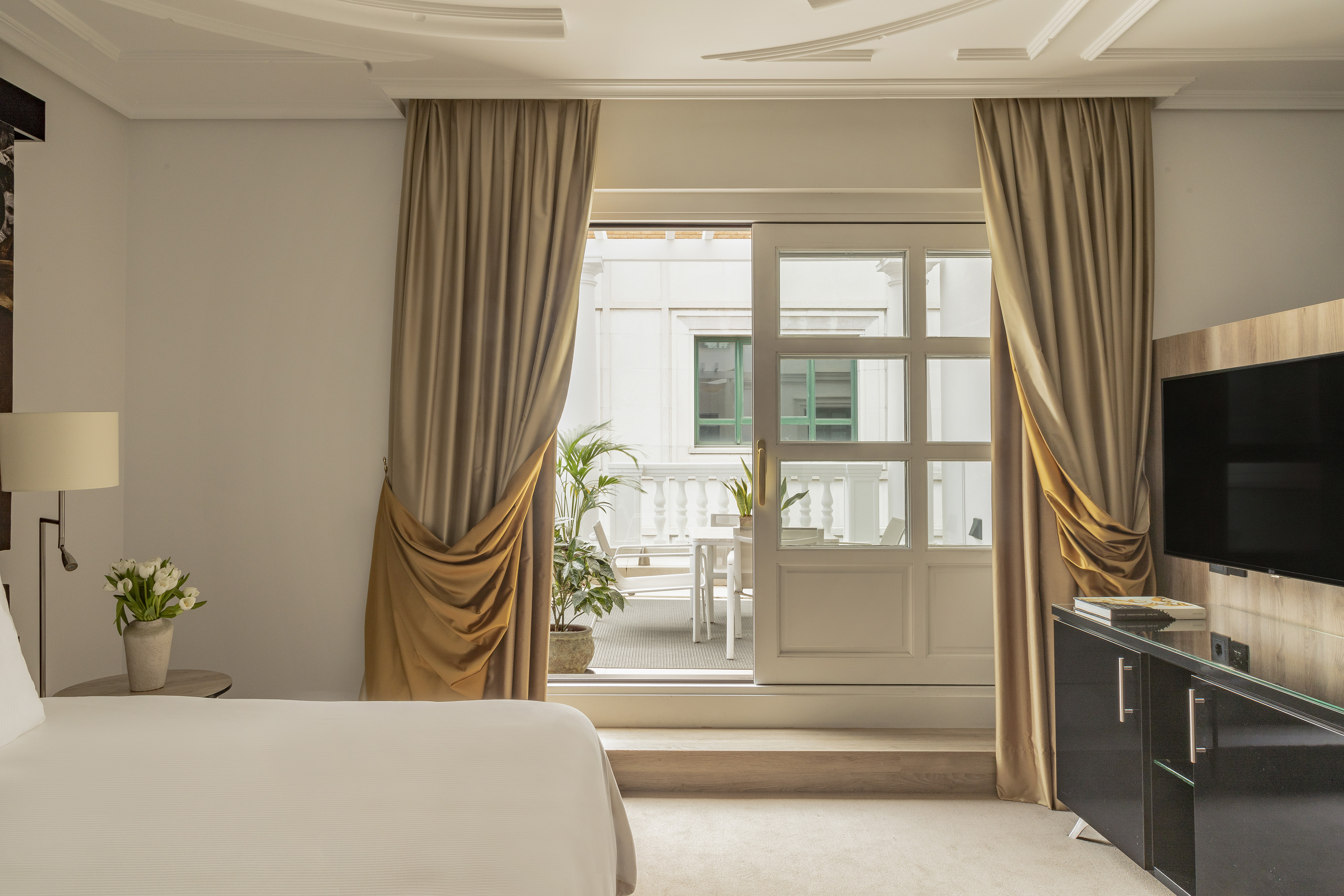 Hotel bedroom with private balcony, outdoor seating, and elegant decor.