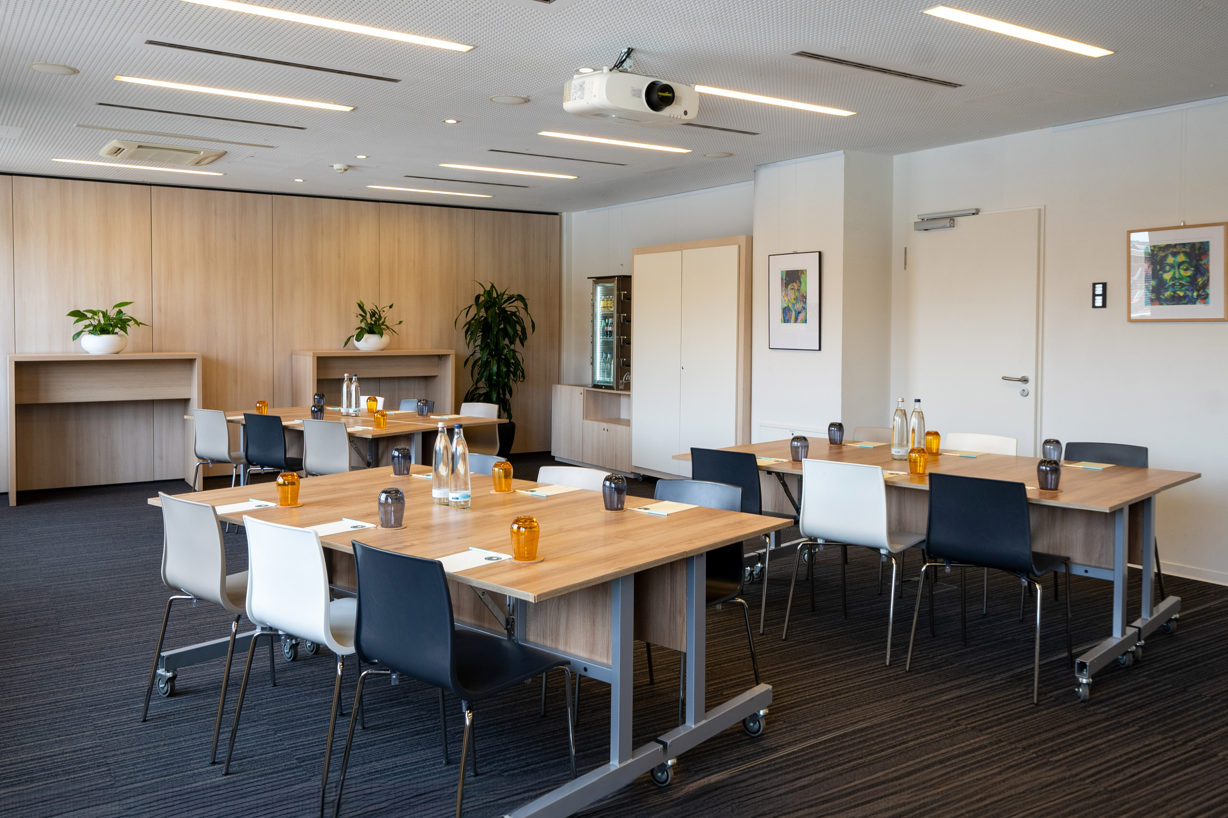 Modern conference meeting room with projector, tables, chairs, and wood paneling.
