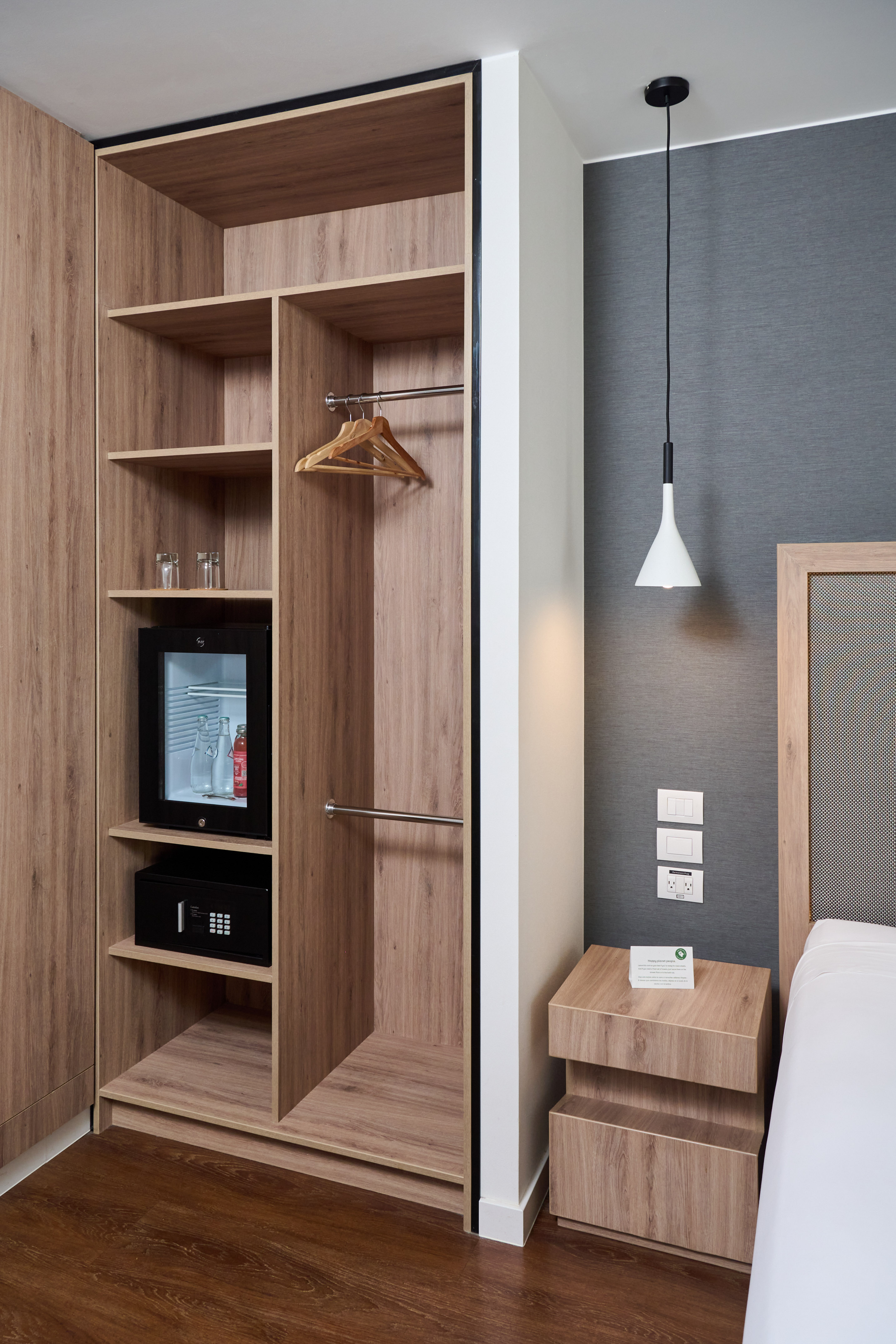 Wooden hotel wardrobe with mini-bar, safe, and modern bedside table.