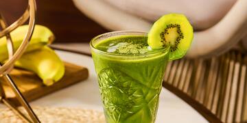 a person pouring a kiwi into a glass of drink