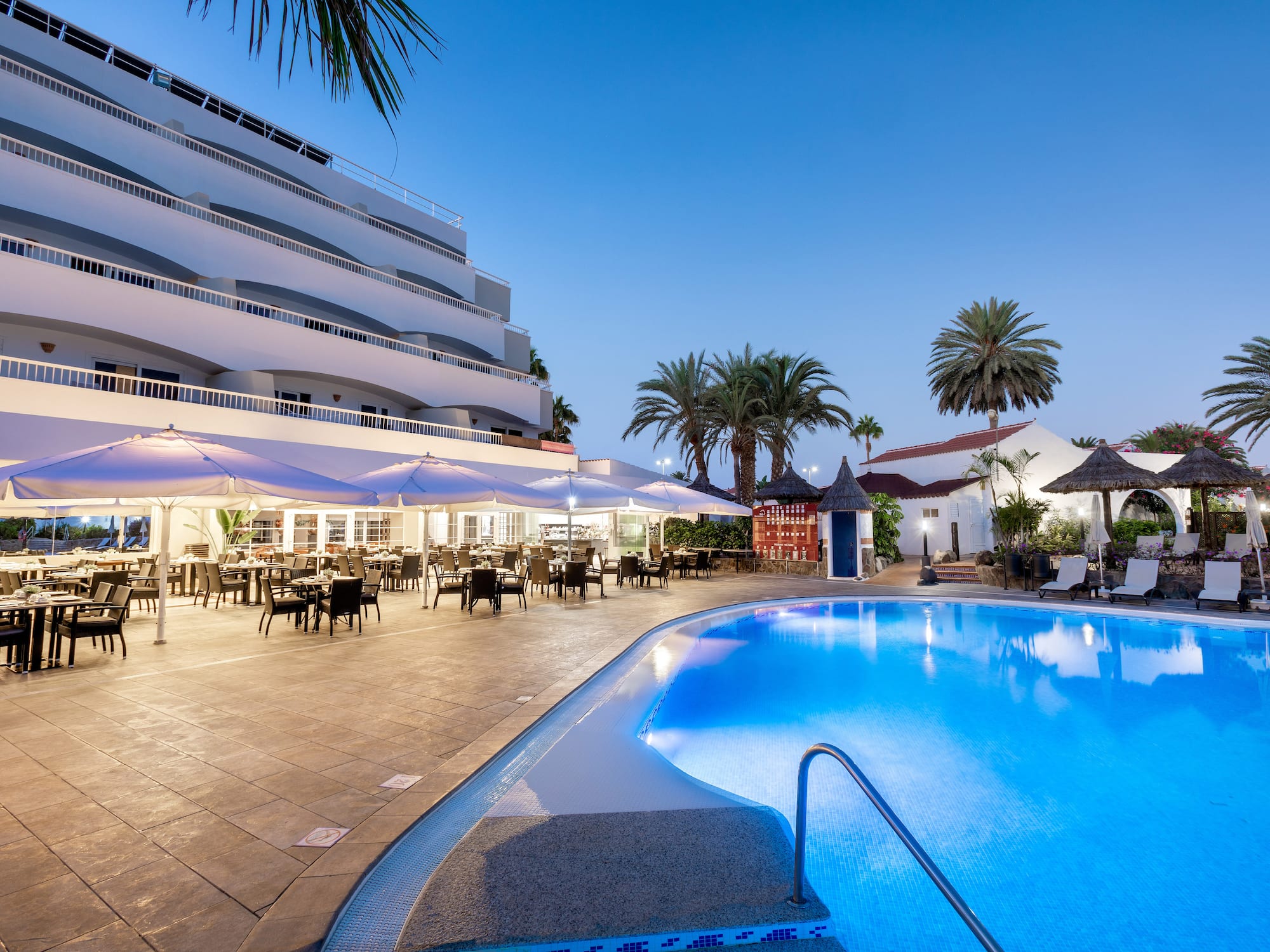 Resort hotel pool, outdoor dining, and palm trees at dusk.
