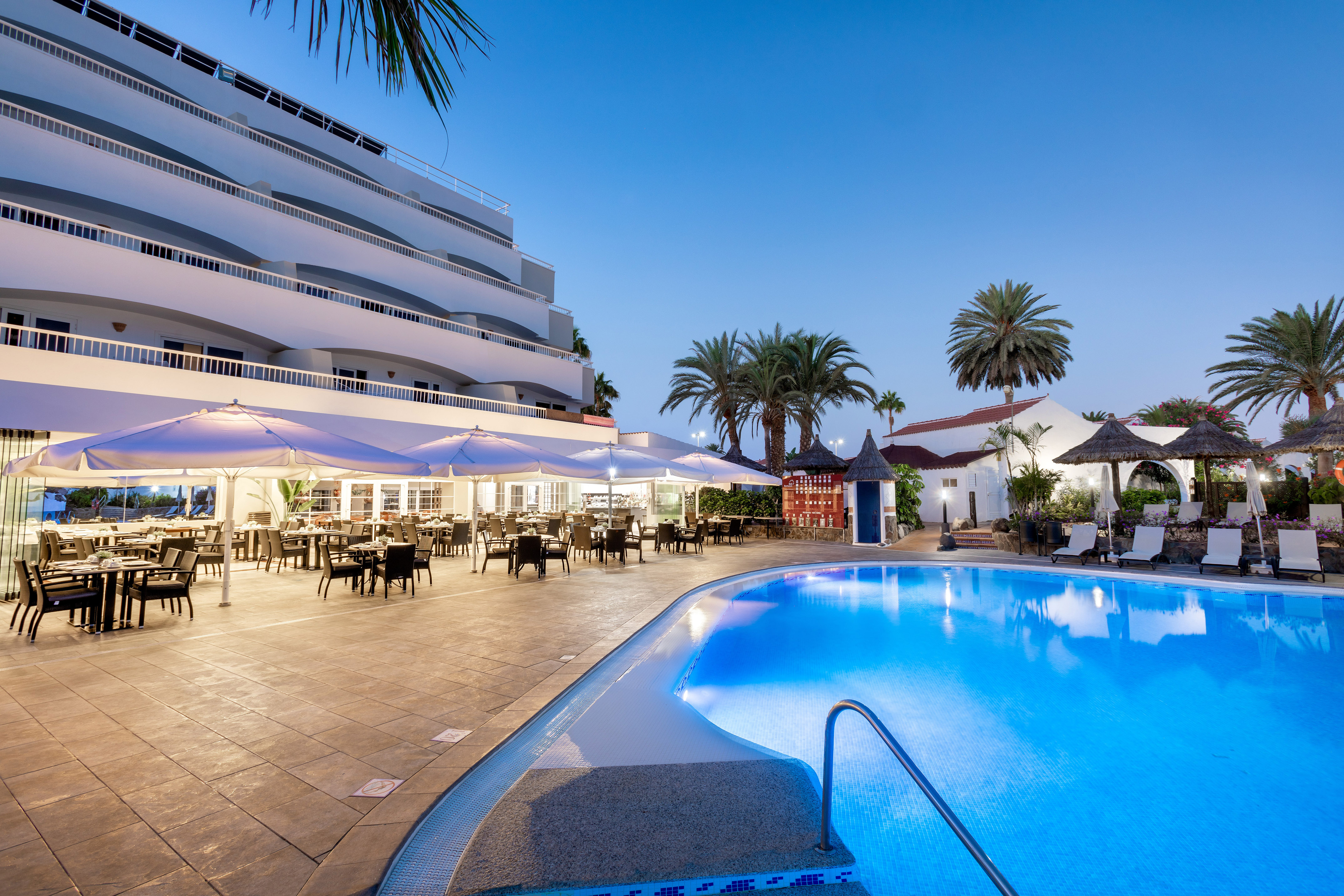 Resort hotel pool, outdoor dining, and palm trees at dusk.