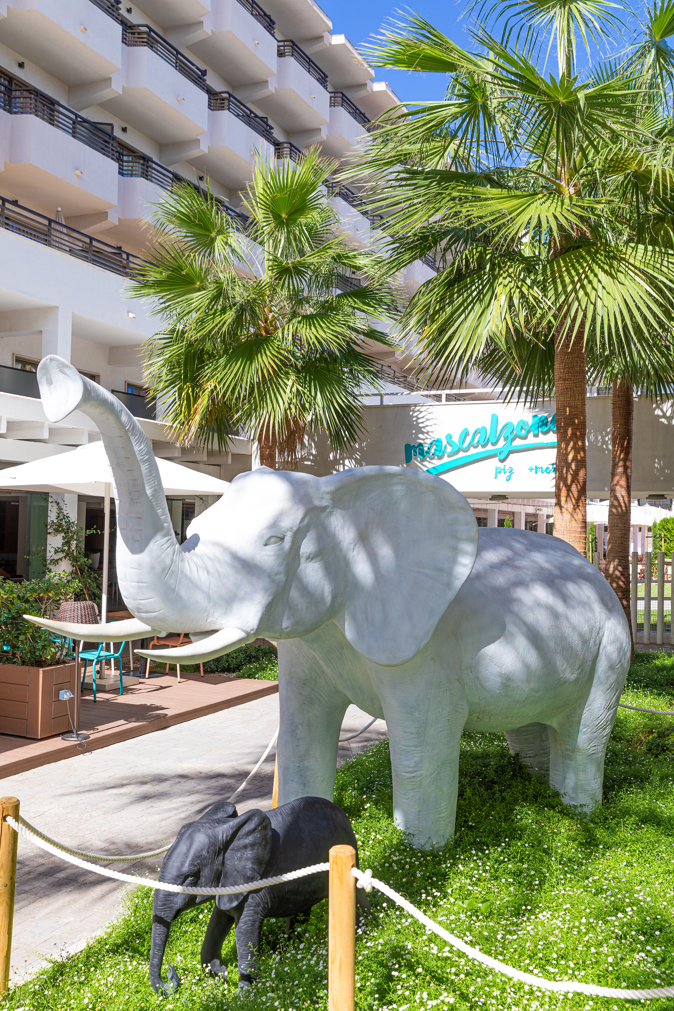 White and black elephant statues in a tropical hotel garden with palm trees.