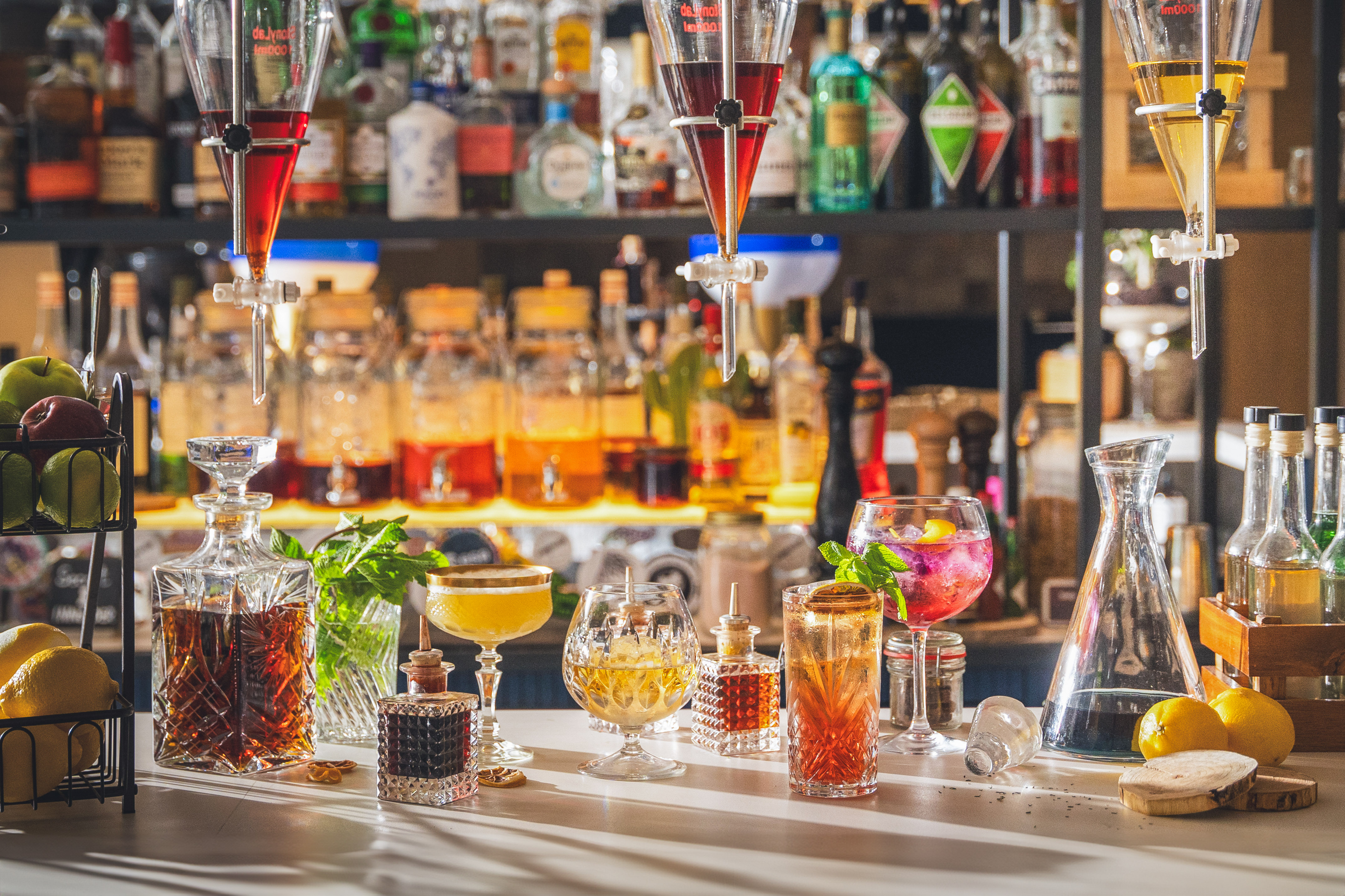 Bar counter with colorful cocktails, decanters, and liquor bottles.