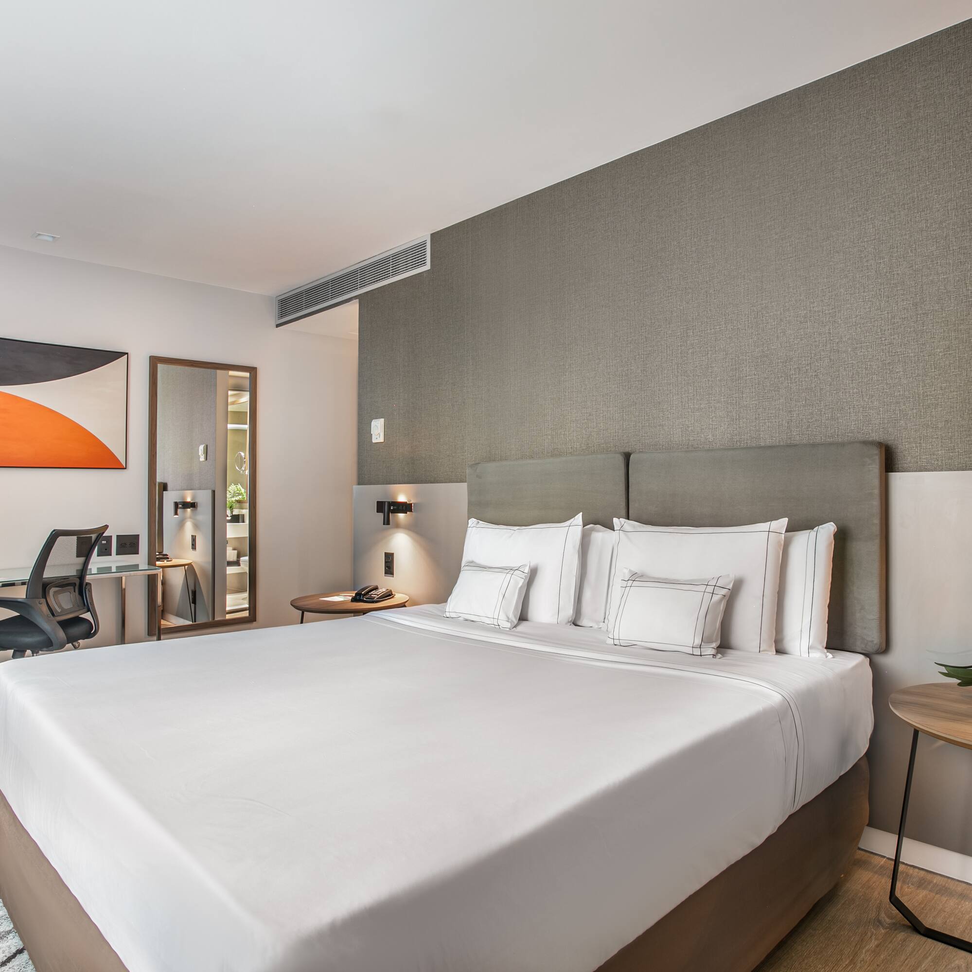 a bed with white sheets and a table with lamp and chair