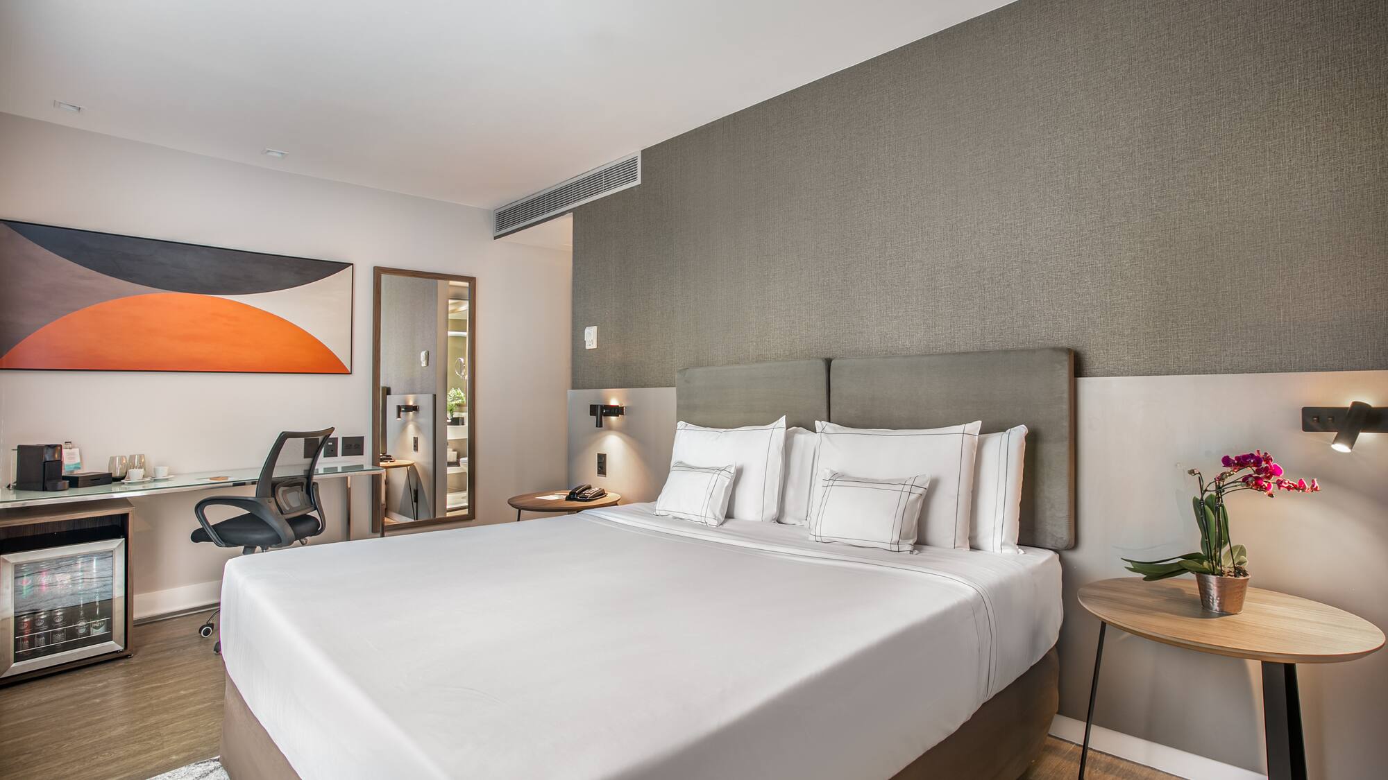 a bed with white sheets and a table with lamp and chair