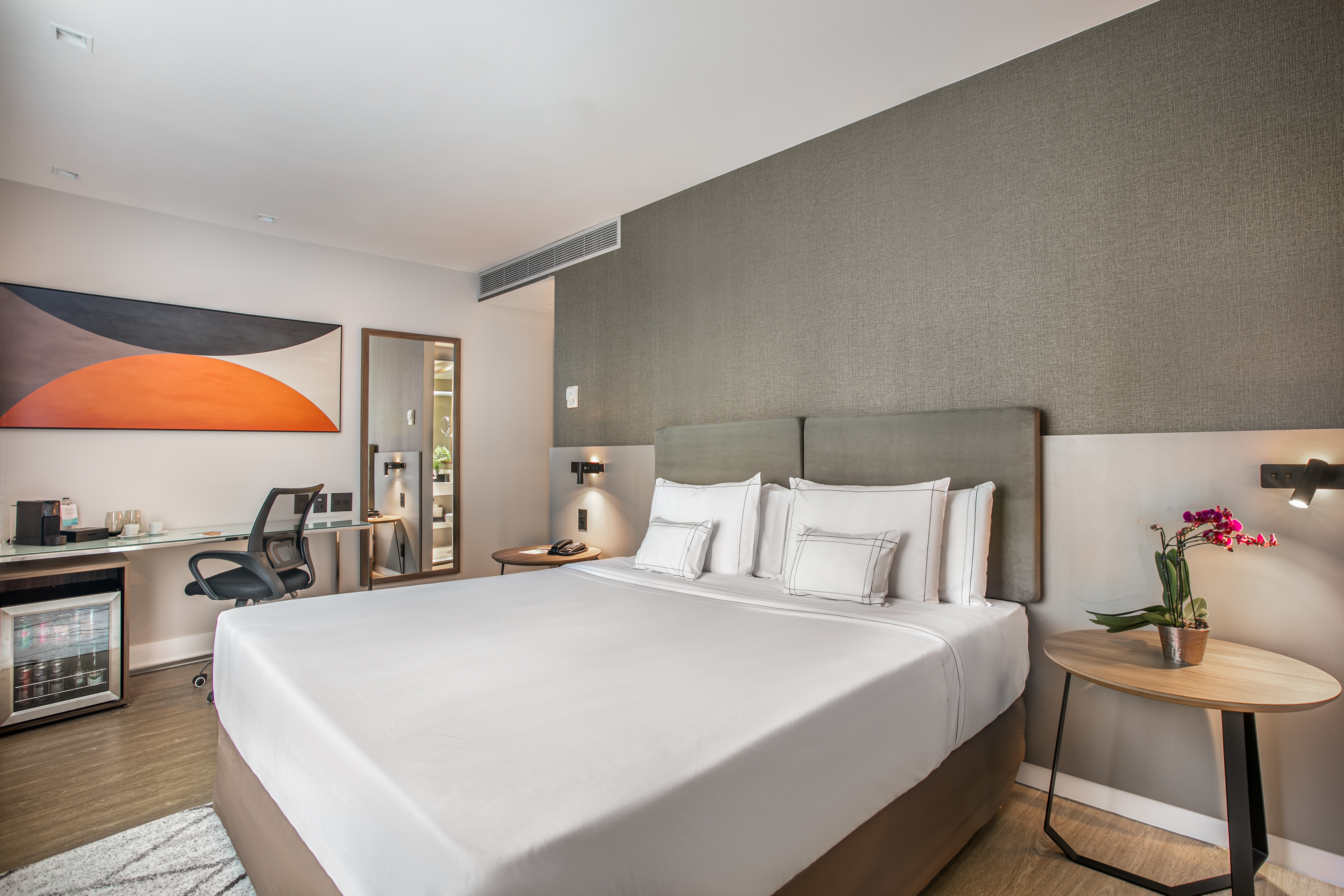 Modern hotel room with king bed, desk, minibar, and stylish contemporary decor.