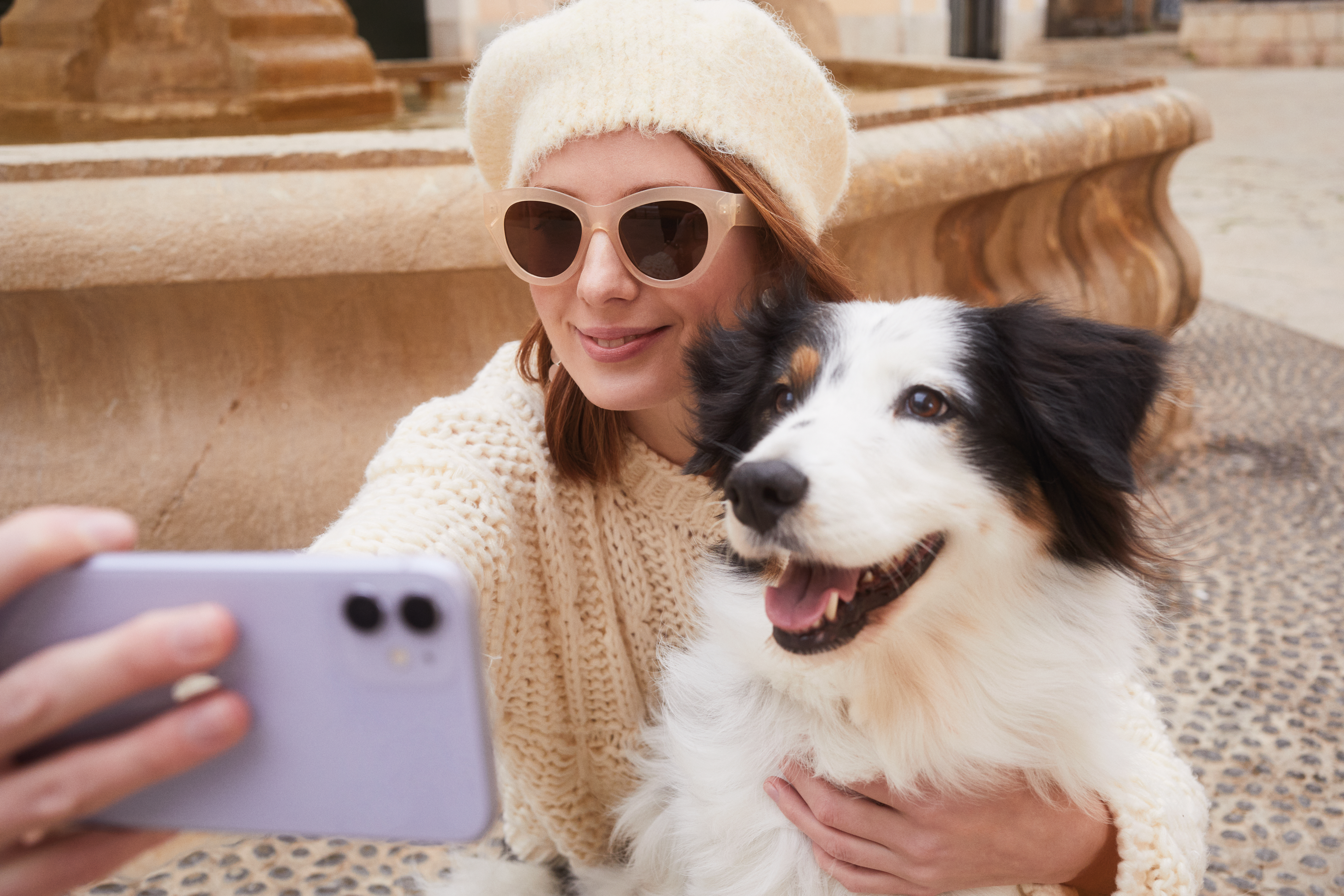 Woman in beret and sunglasses taking a selfie with happy dog.