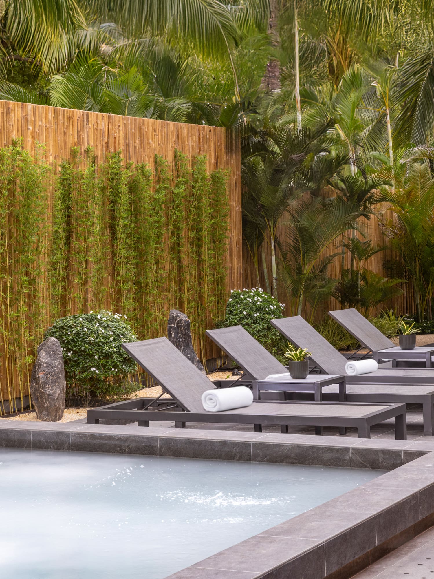 Tropical hot tub area with lounge chairs and bamboo privacy fence.