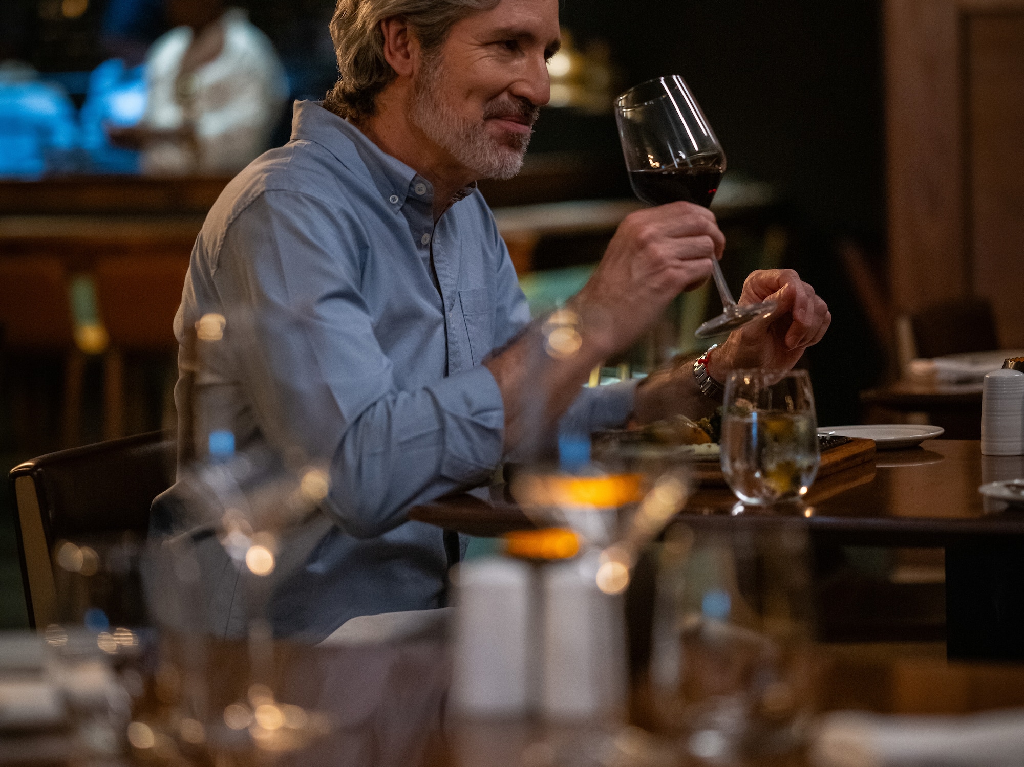 Hombre canoso sonriendo con copa de vino tinto en restaurante elegante.