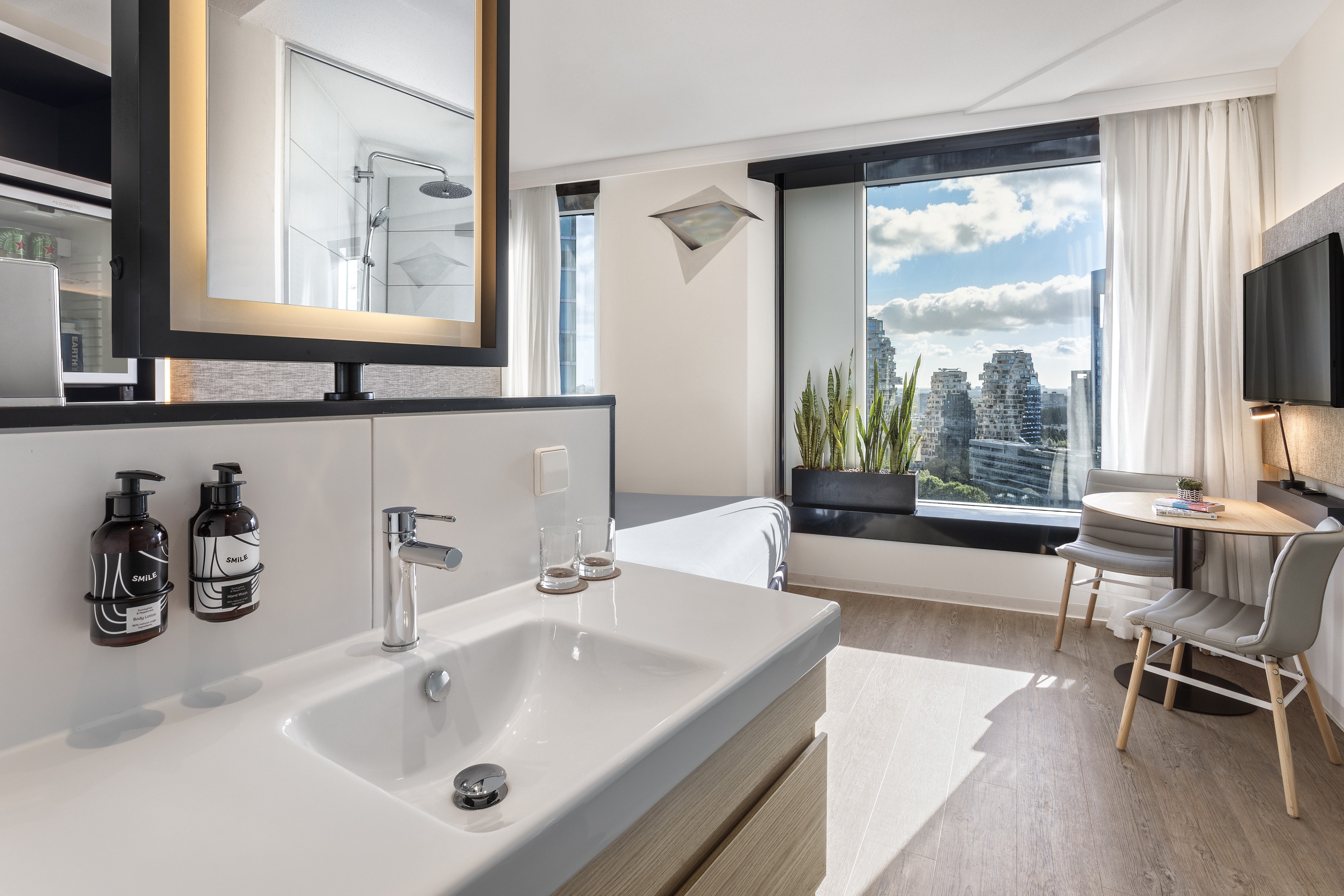 Contemporary hotel room with vanity, city view window, and dining table.