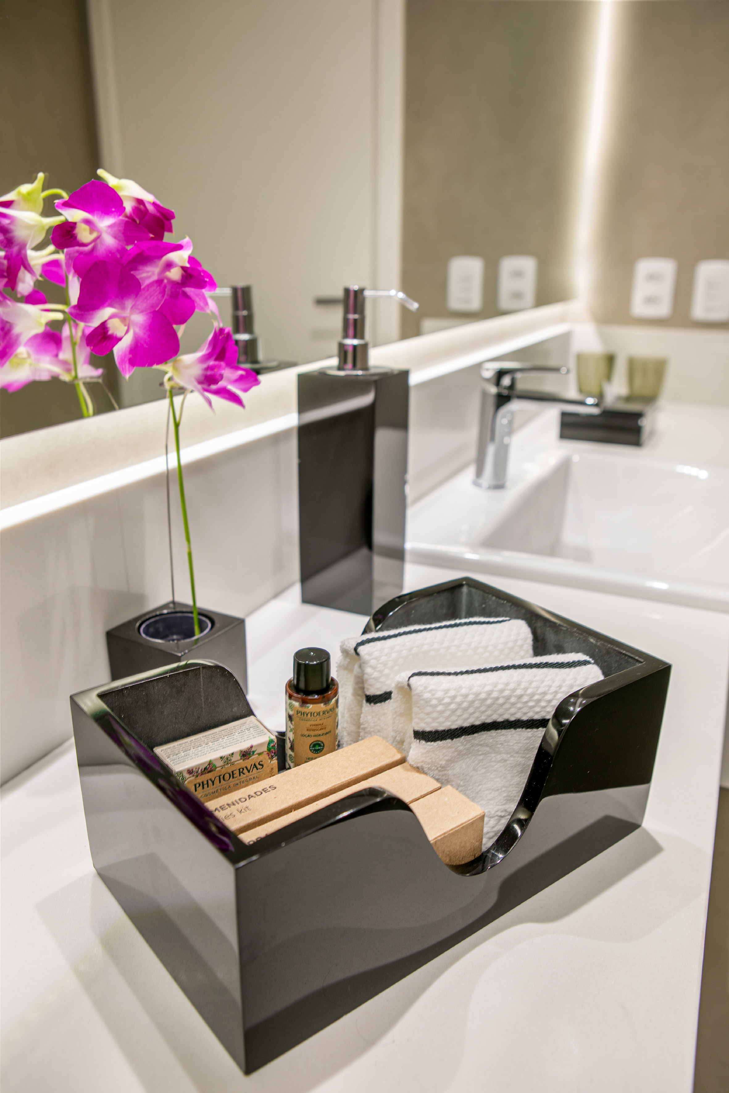 Hotel bathroom vanity with pink orchids, amenities, soap, and towels.