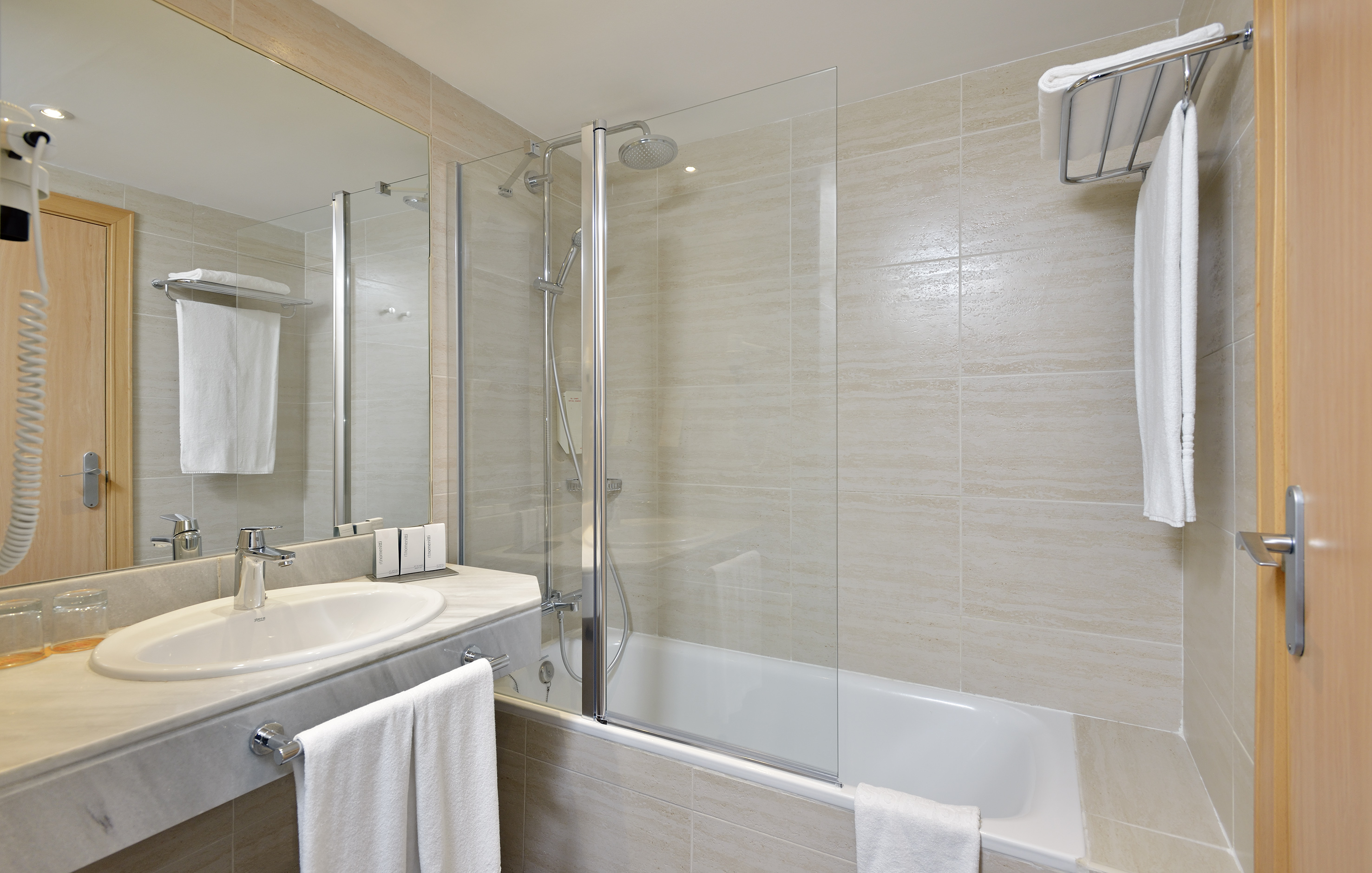 Modern hotel bathroom with bathtub, shower, sink, mirror, and white towels.