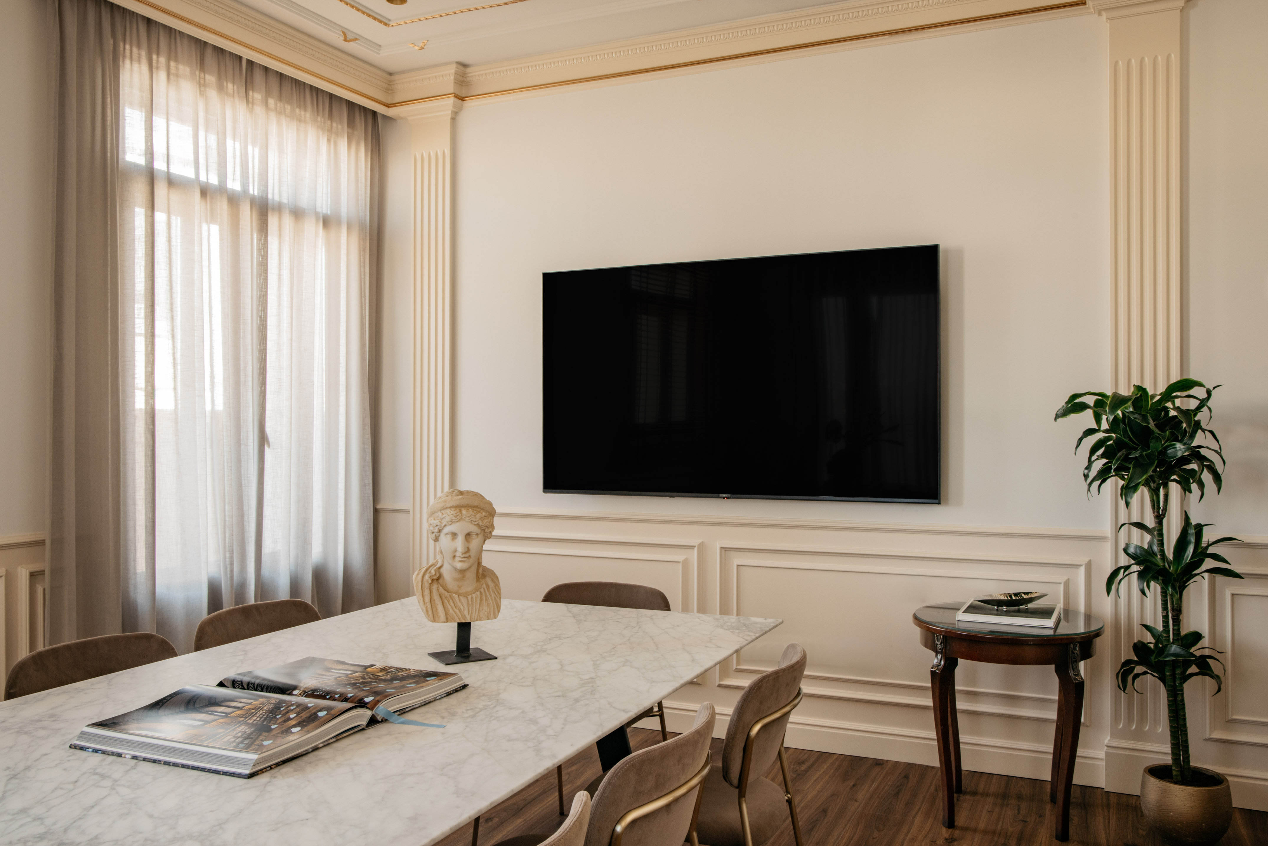 Modern dining room with marble table, mounted TV, Roman bust, and architectural trim.
