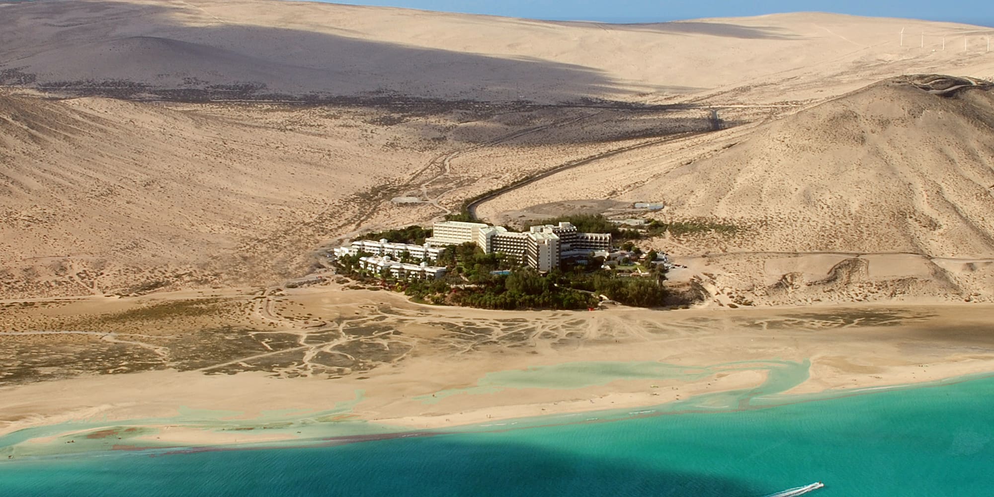 Aerial view of resort hotel on sandy beach with turquoise ocean and vast dunes.