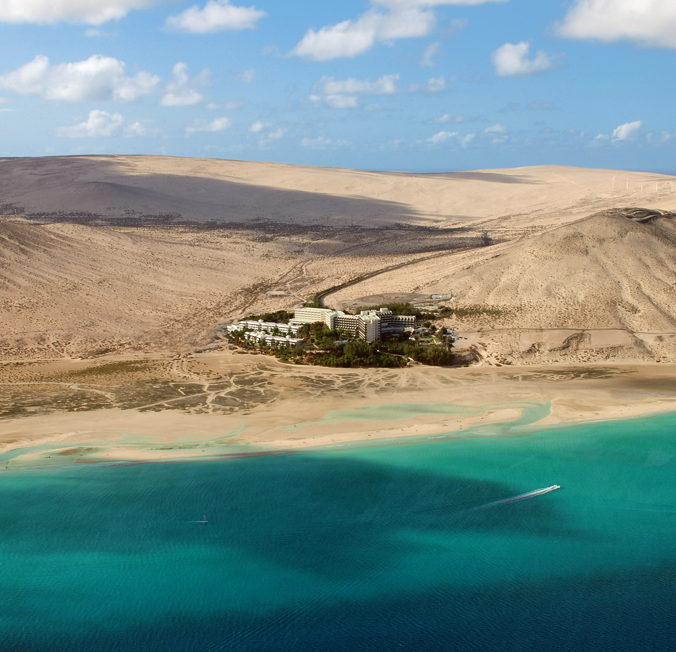 Aerial view of resort hotel on sandy beach with turquoise ocean and vast dunes.