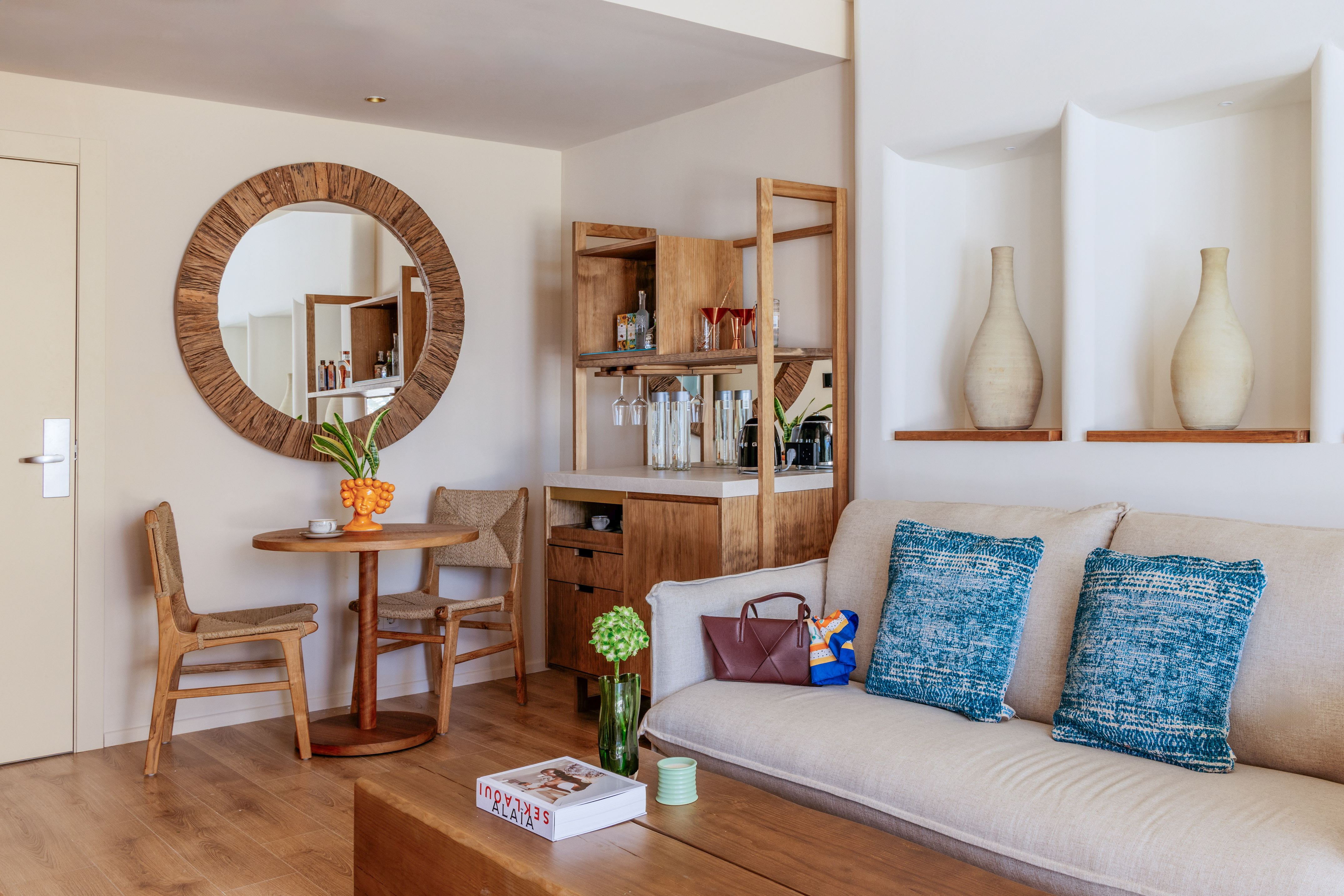 Bright modern living room with wooden bar, beige sofa, and large round mirror.