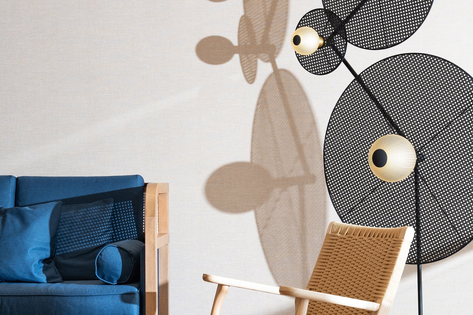 Modern living room: blue sofa, woven armchair, perforated lamp, jute rug.