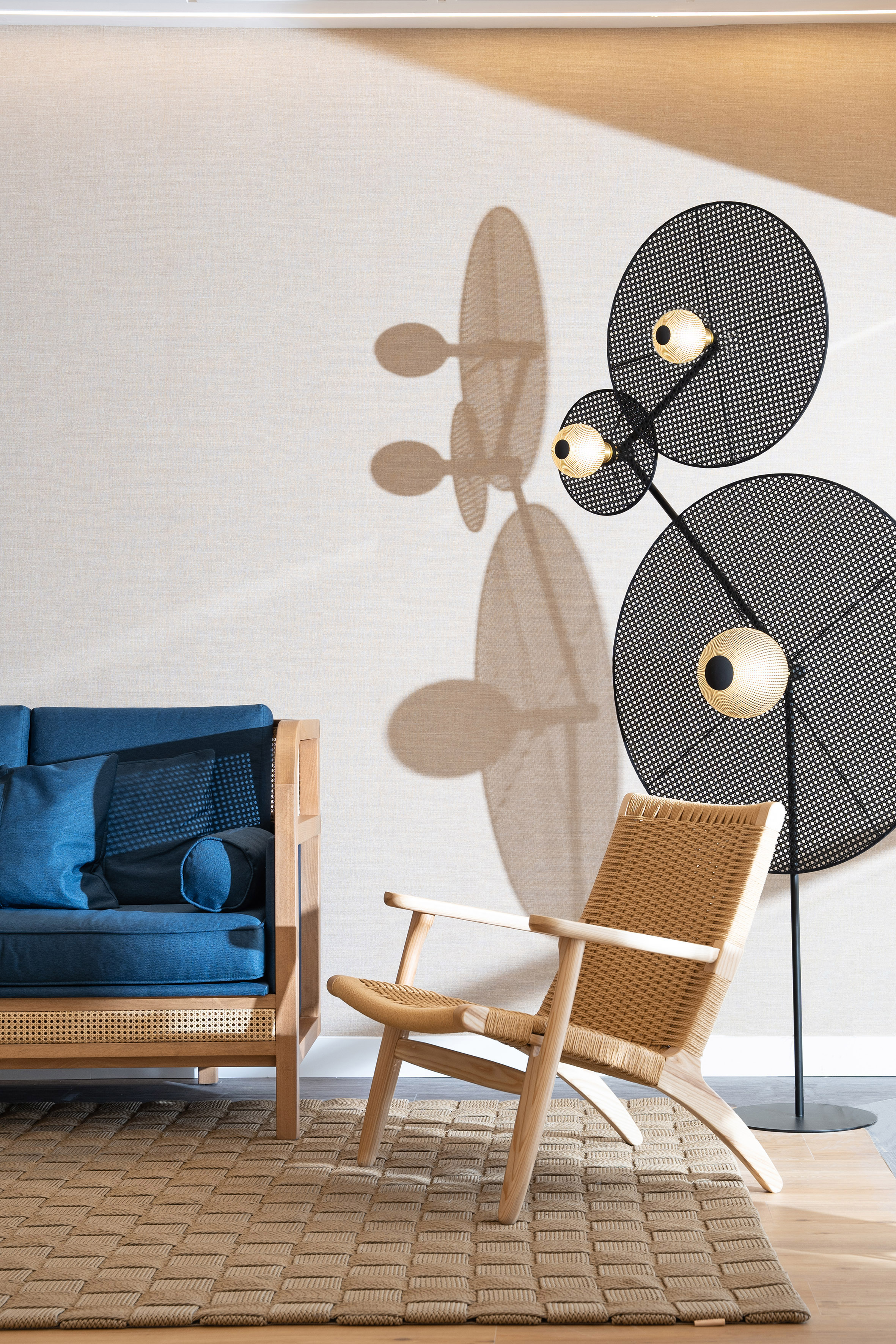 Modern living room: blue sofa, woven armchair, perforated lamp, jute rug.