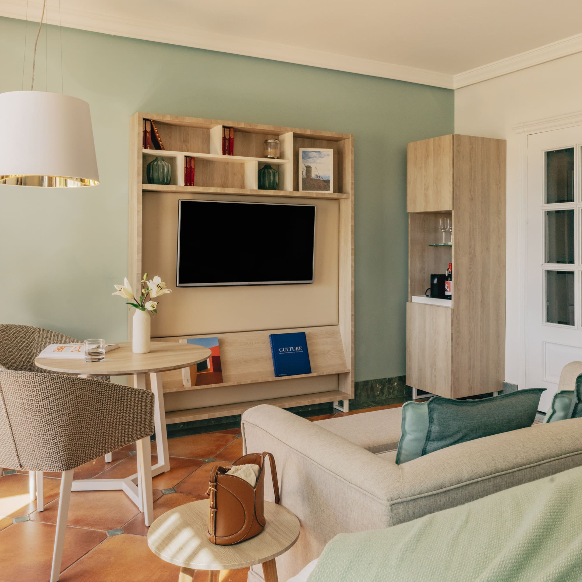 Hotel suite with green walls, terracotta floor, TV, comfortable sofa, and dining area.