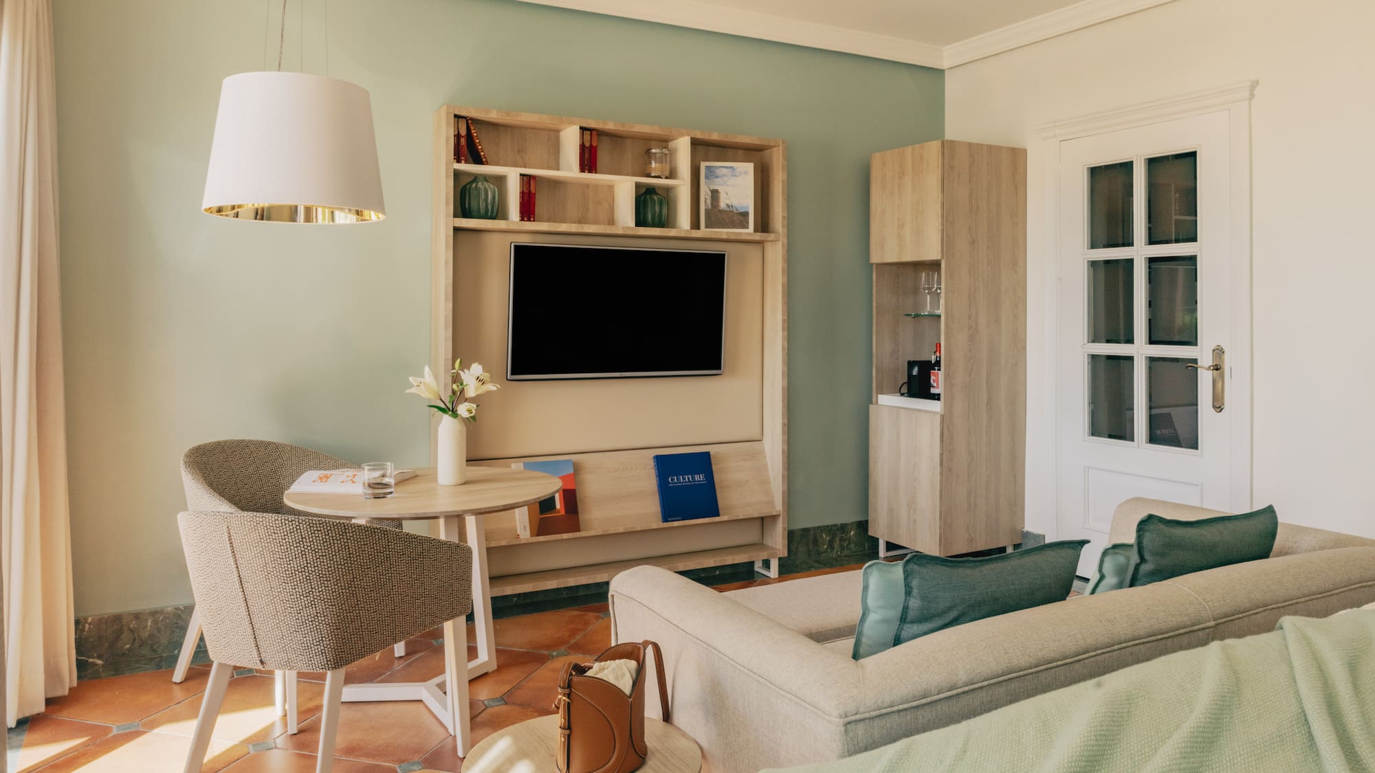 Hotel suite with green walls, terracotta floor, TV, comfortable sofa, and dining area.