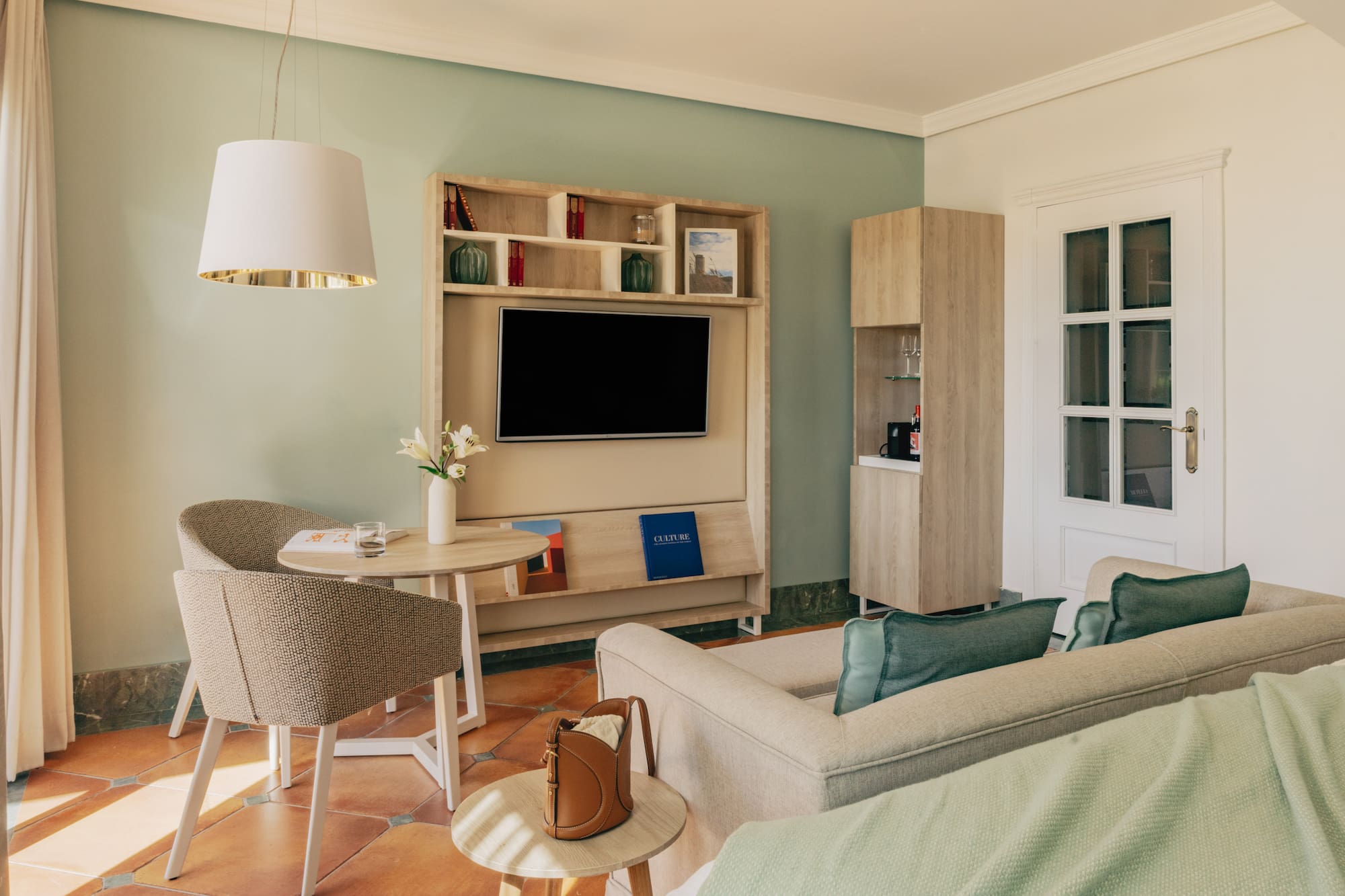 Hotel suite with green walls, terracotta floor, TV, comfortable sofa, and dining area.