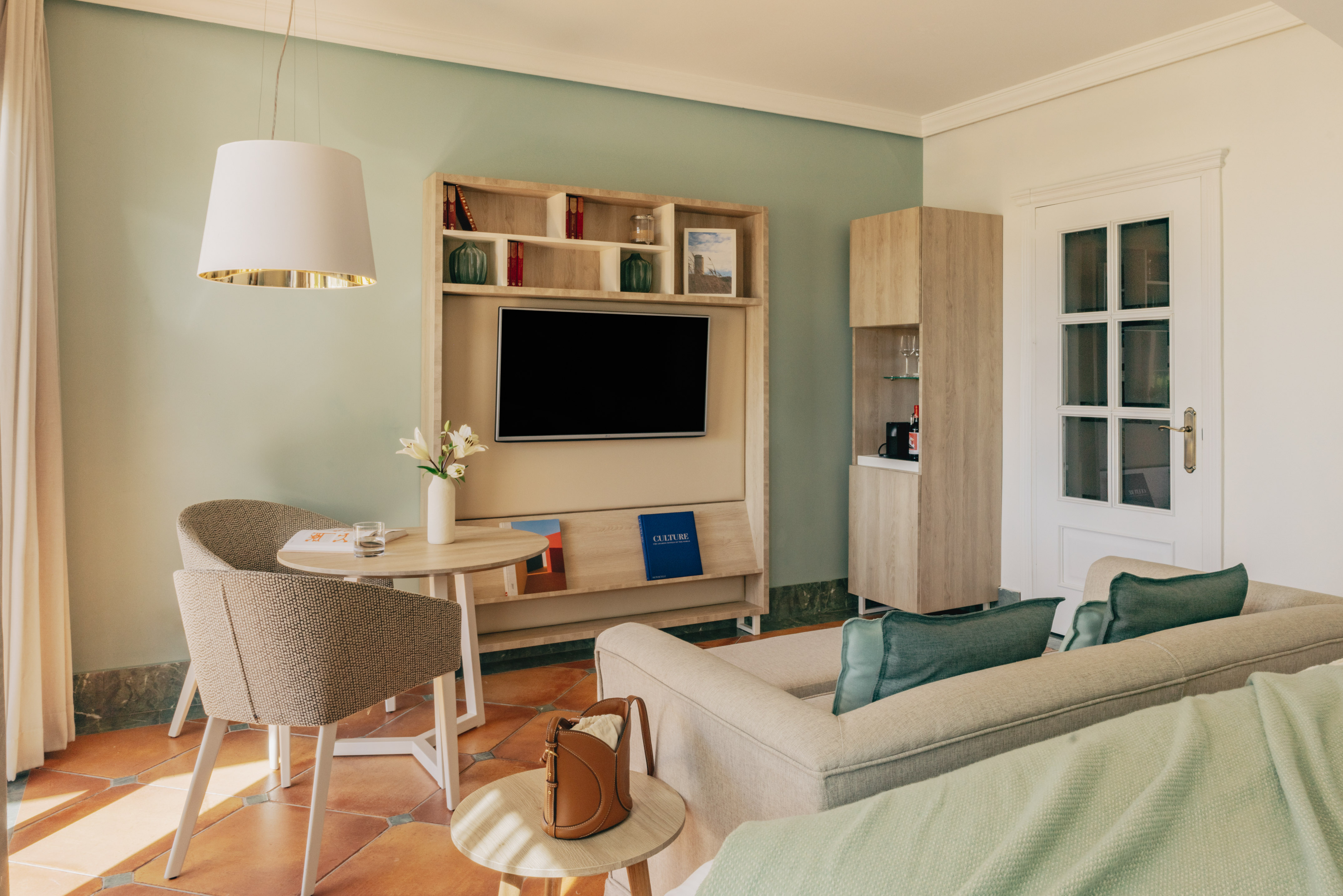 Hotel suite with green walls, terracotta floor, TV, comfortable sofa, and dining area.