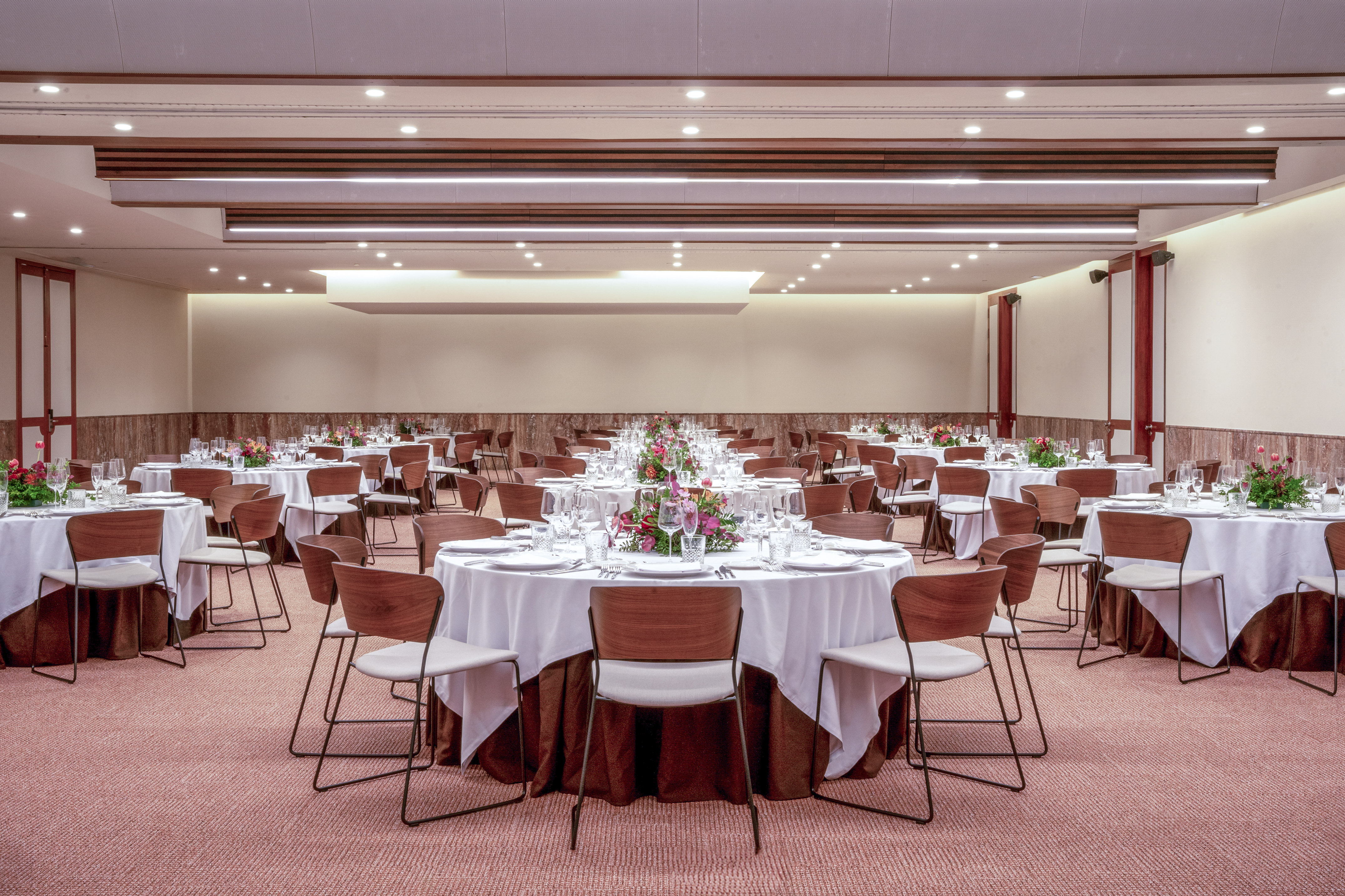 Modern banquet hall with round tables, chairs, and floral centerpieces.