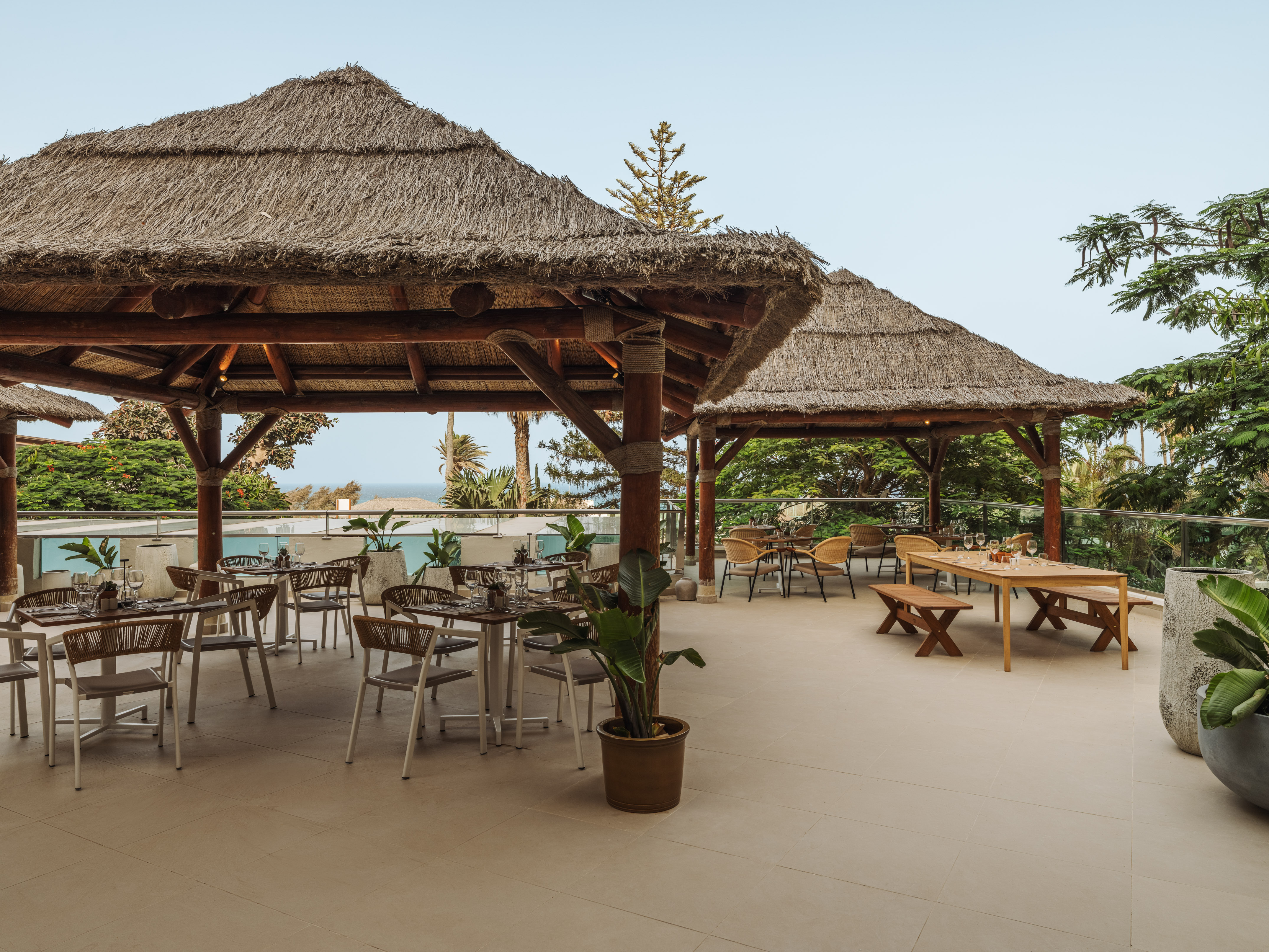 Thatched roof outdoor restaurant patio with tables and distant ocean view.