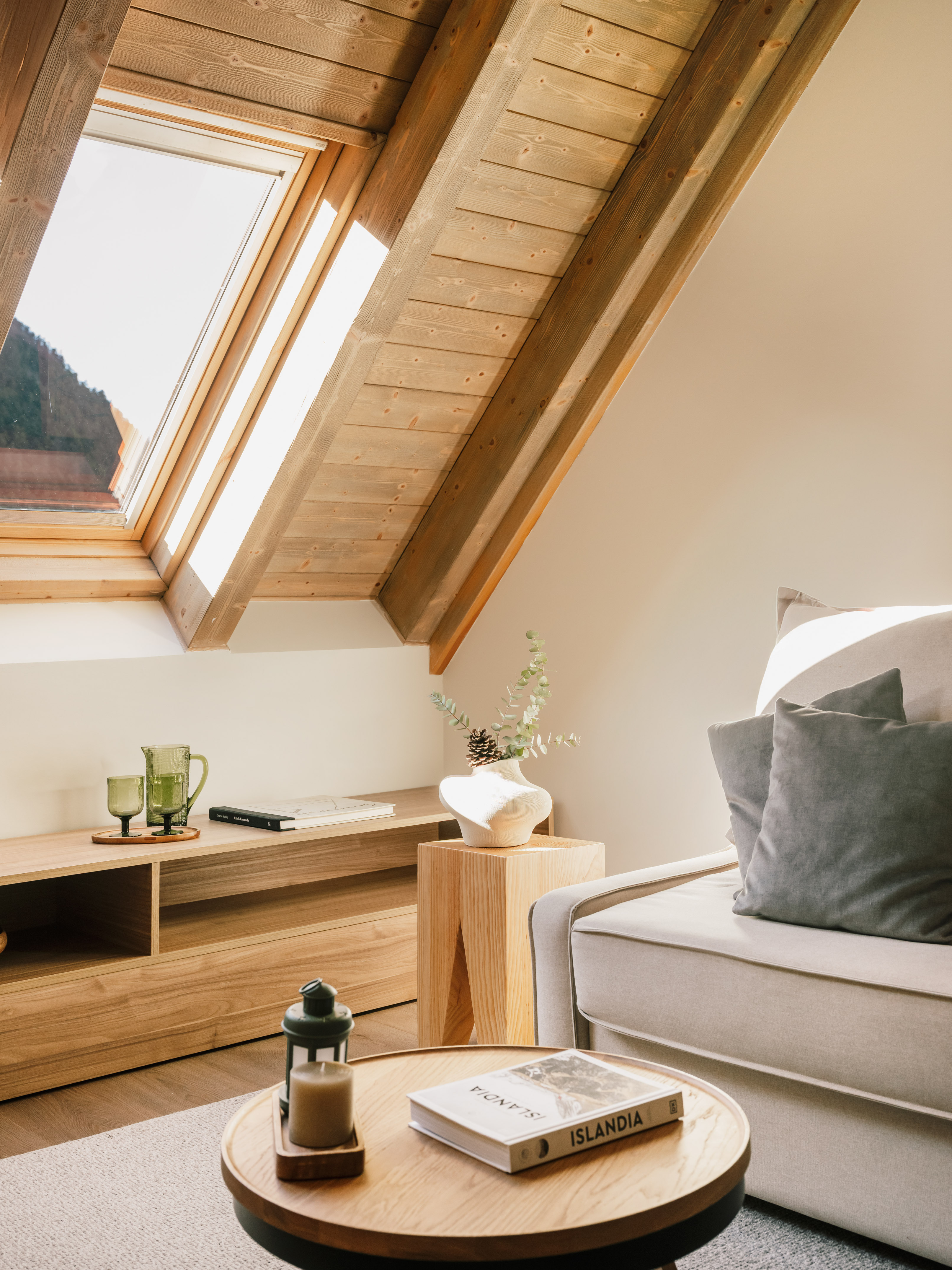Sloping wooden attic room with bright skylight, cozy sofa, and modern decor.