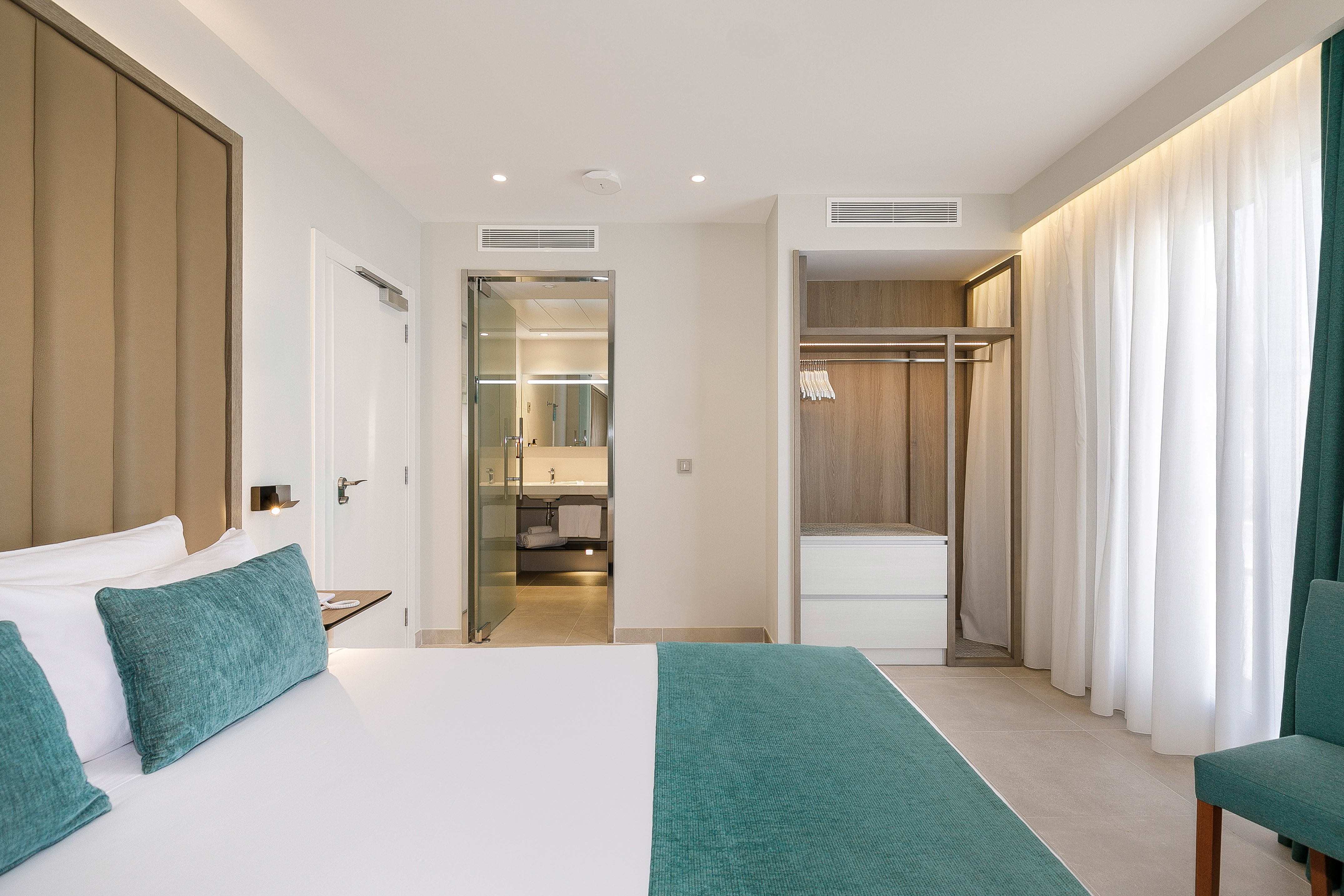 Bright modern hotel room with bed, open wardrobe, and en-suite bathroom.