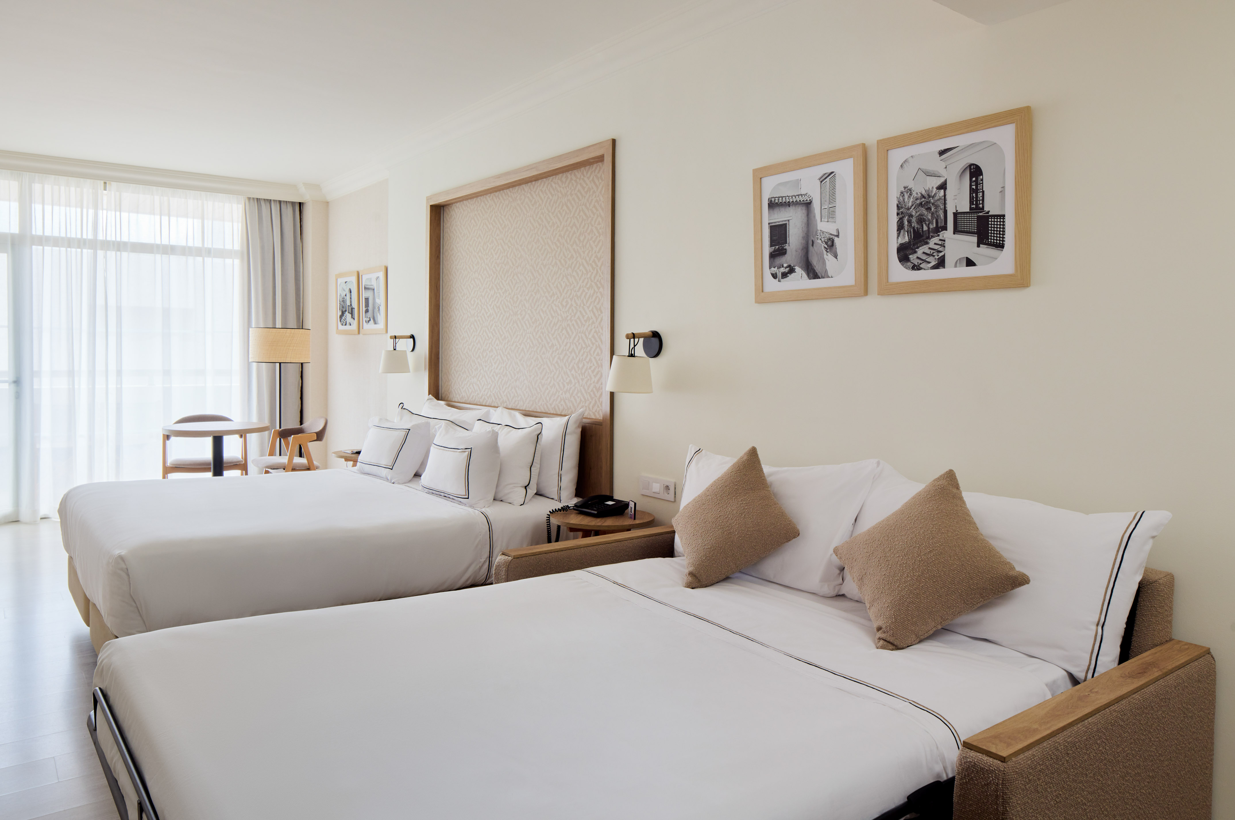 Hotel room with a bed and pull-out sofa bed, white bedding, and bright window.