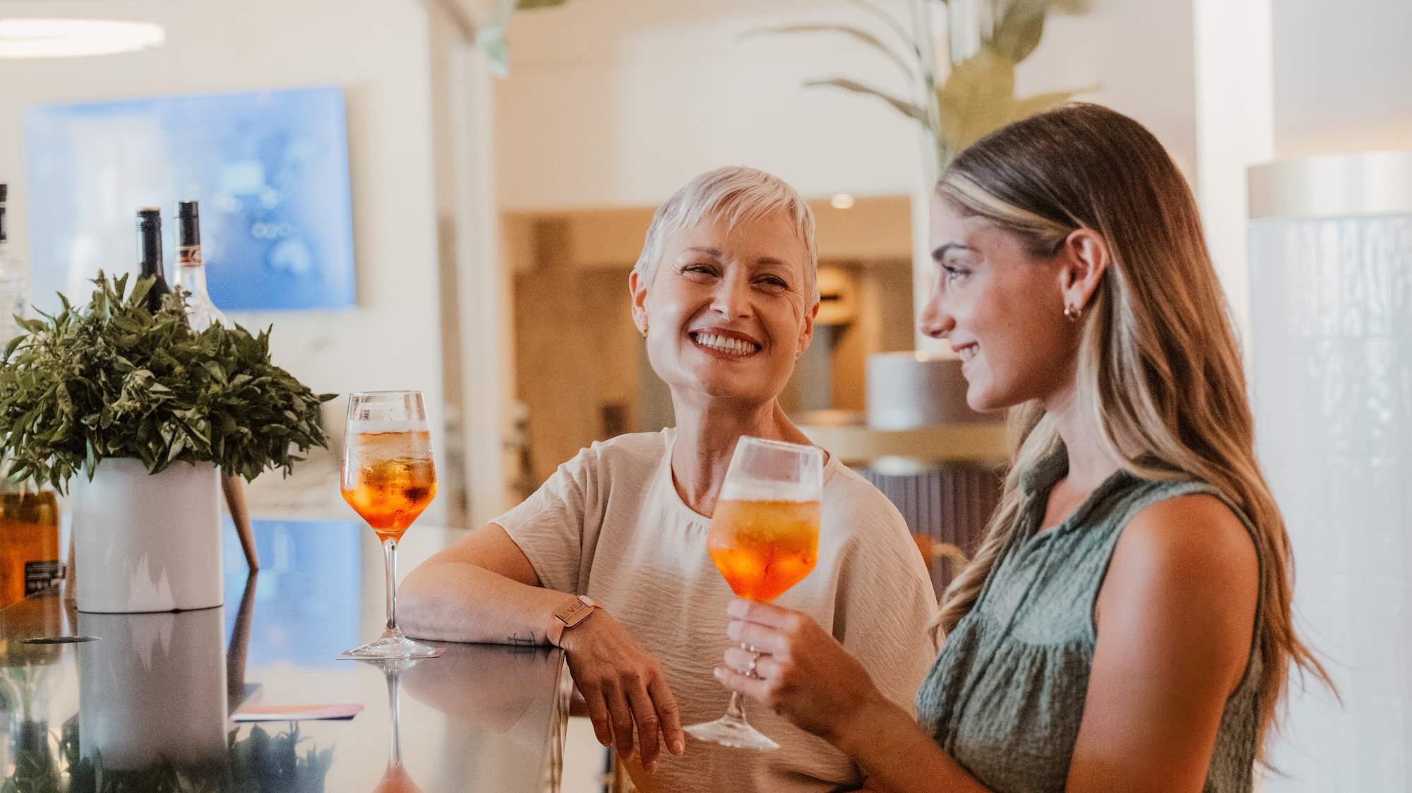a woman sitting at a bar with a woman holding drinks