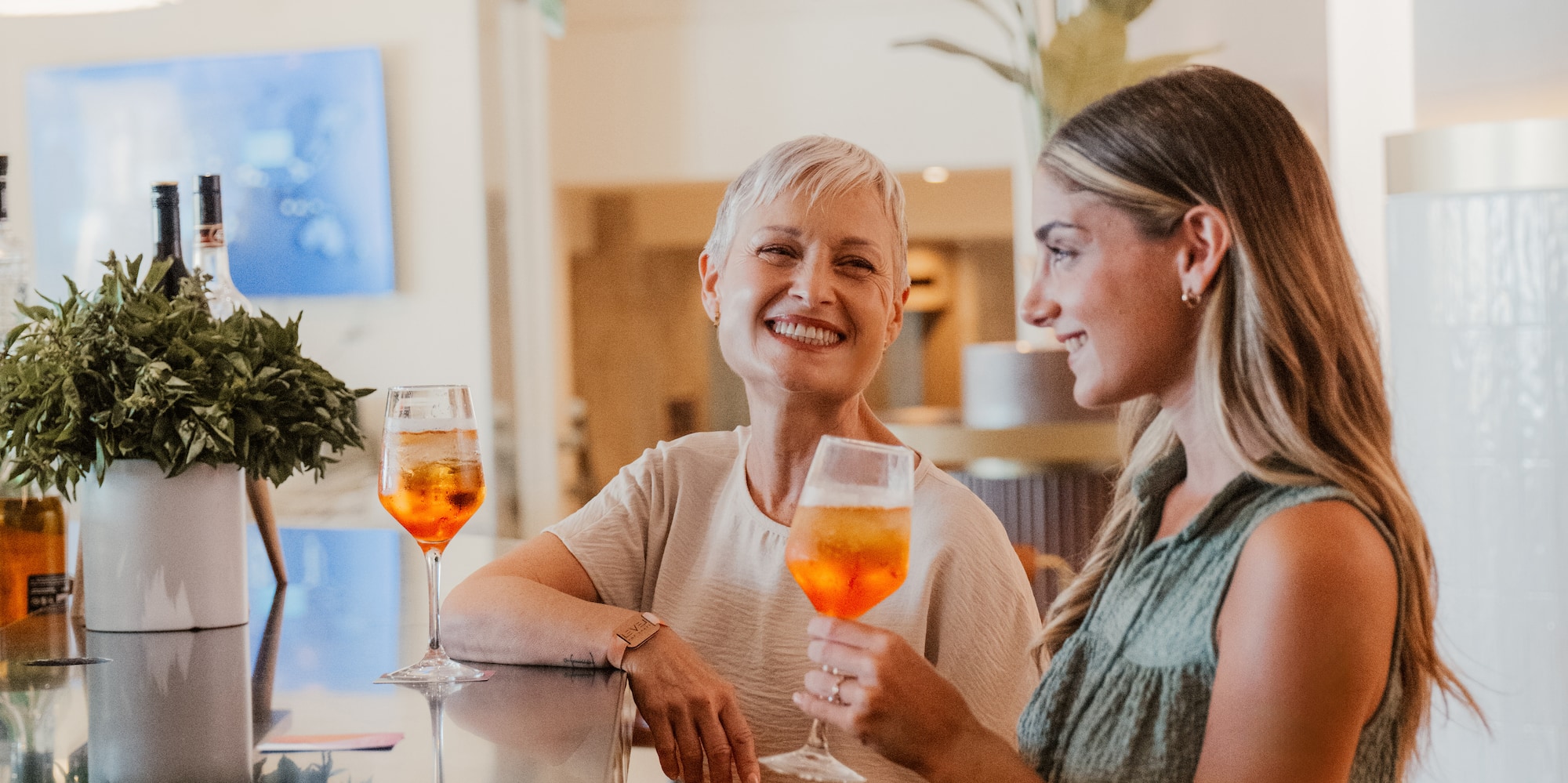a woman sitting at a bar with a woman holding drinks