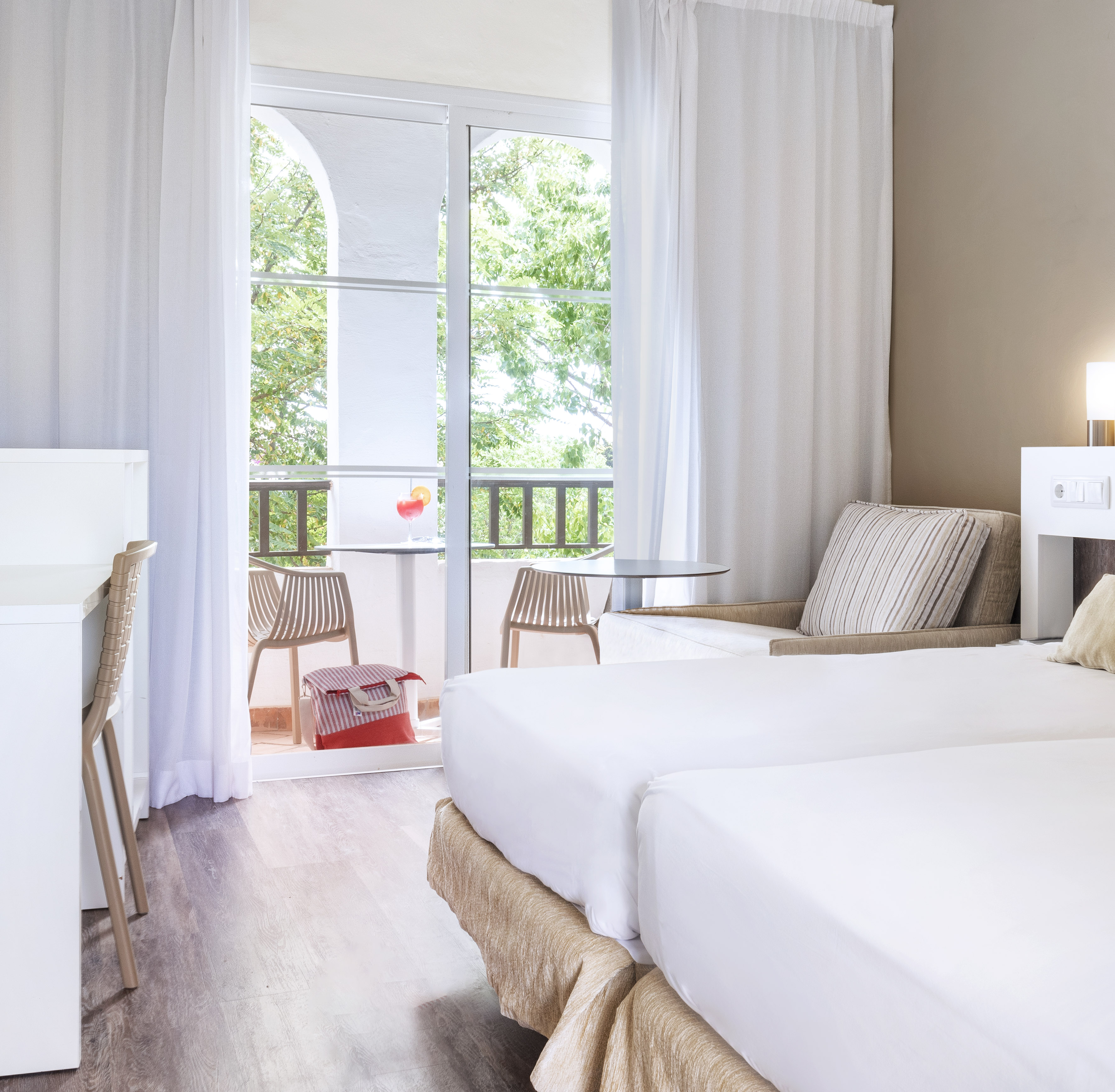 Hotel room with twin beds, desk, and private balcony with outdoor seating.