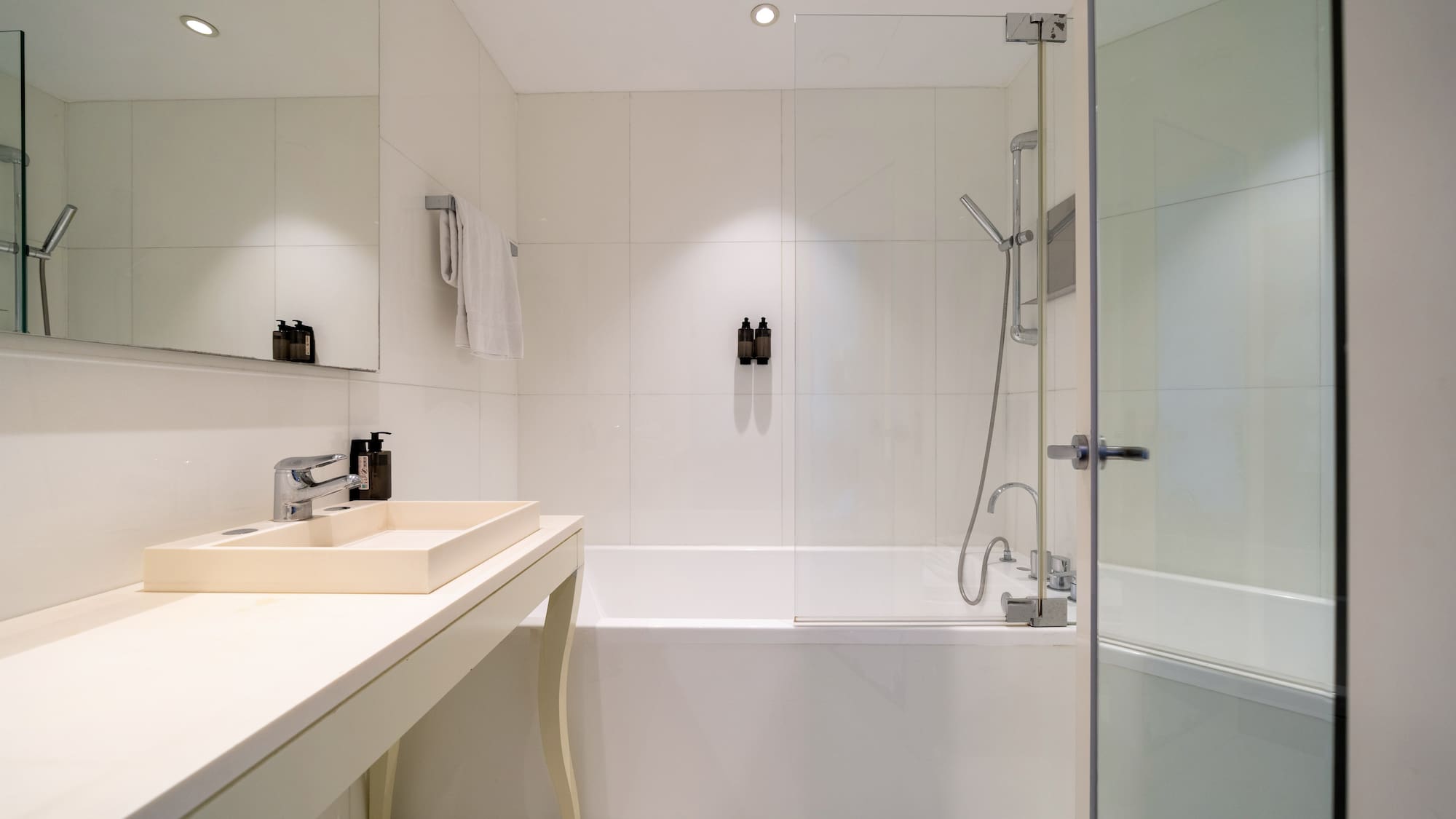 Modern white bathroom with bathtub, glass shower screen, and rectangular sink.