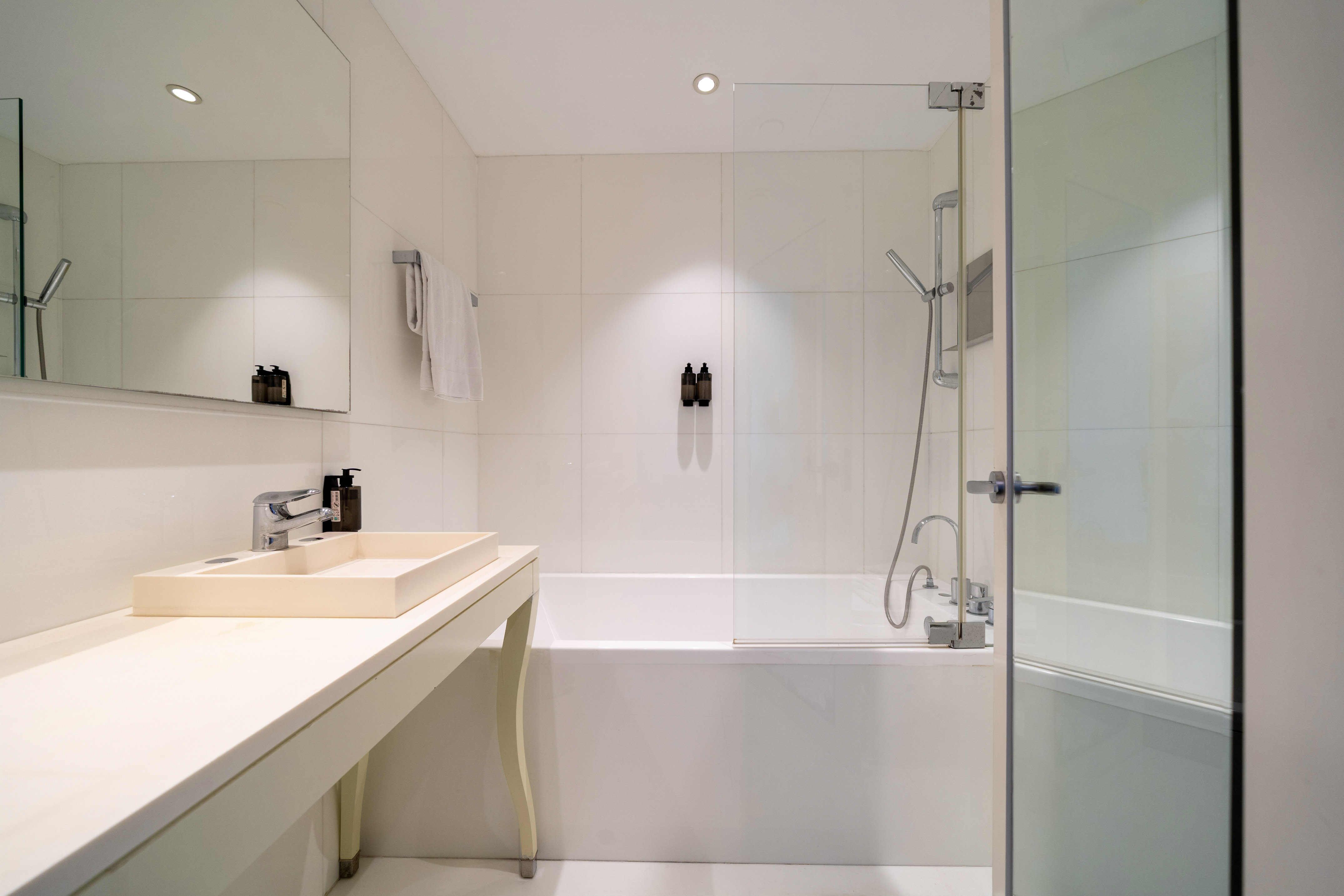 Modern white bathroom with bathtub, glass shower screen, and rectangular sink.