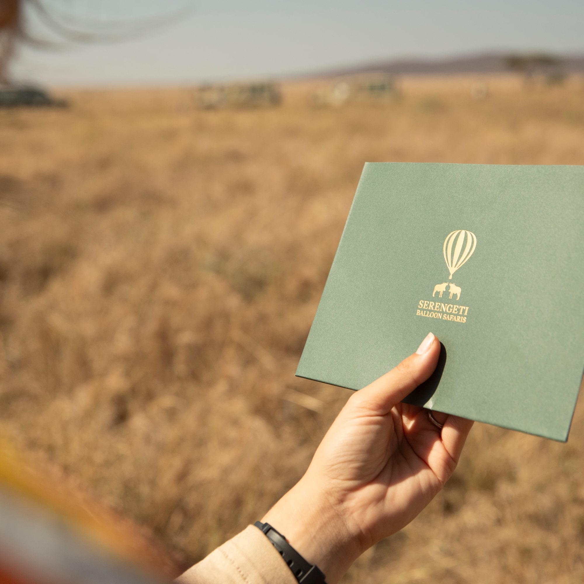 a person holding a green square with a hot air balloon logo