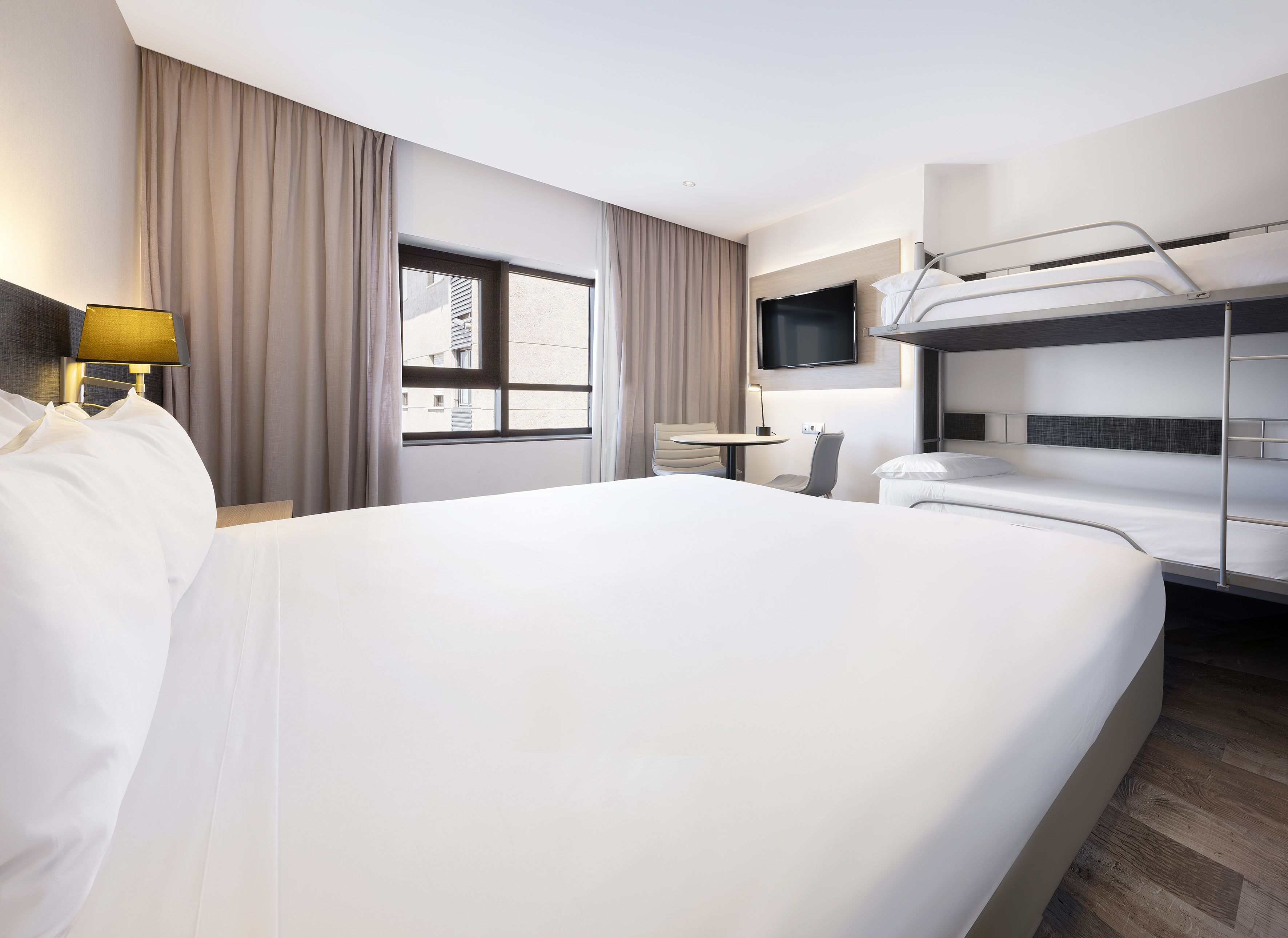 Modern family hotel room with large bed, bunk beds, TV, and window.