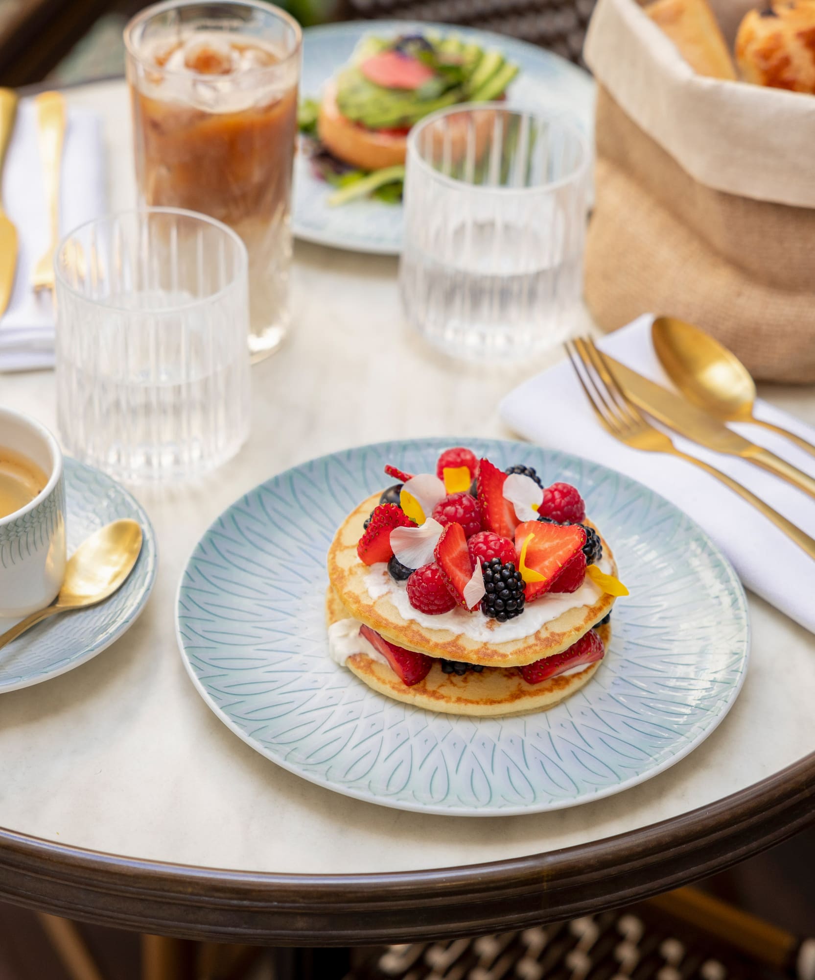 Berry pancakes, espresso, iced coffee, and pastries on an outdoor cafe table.