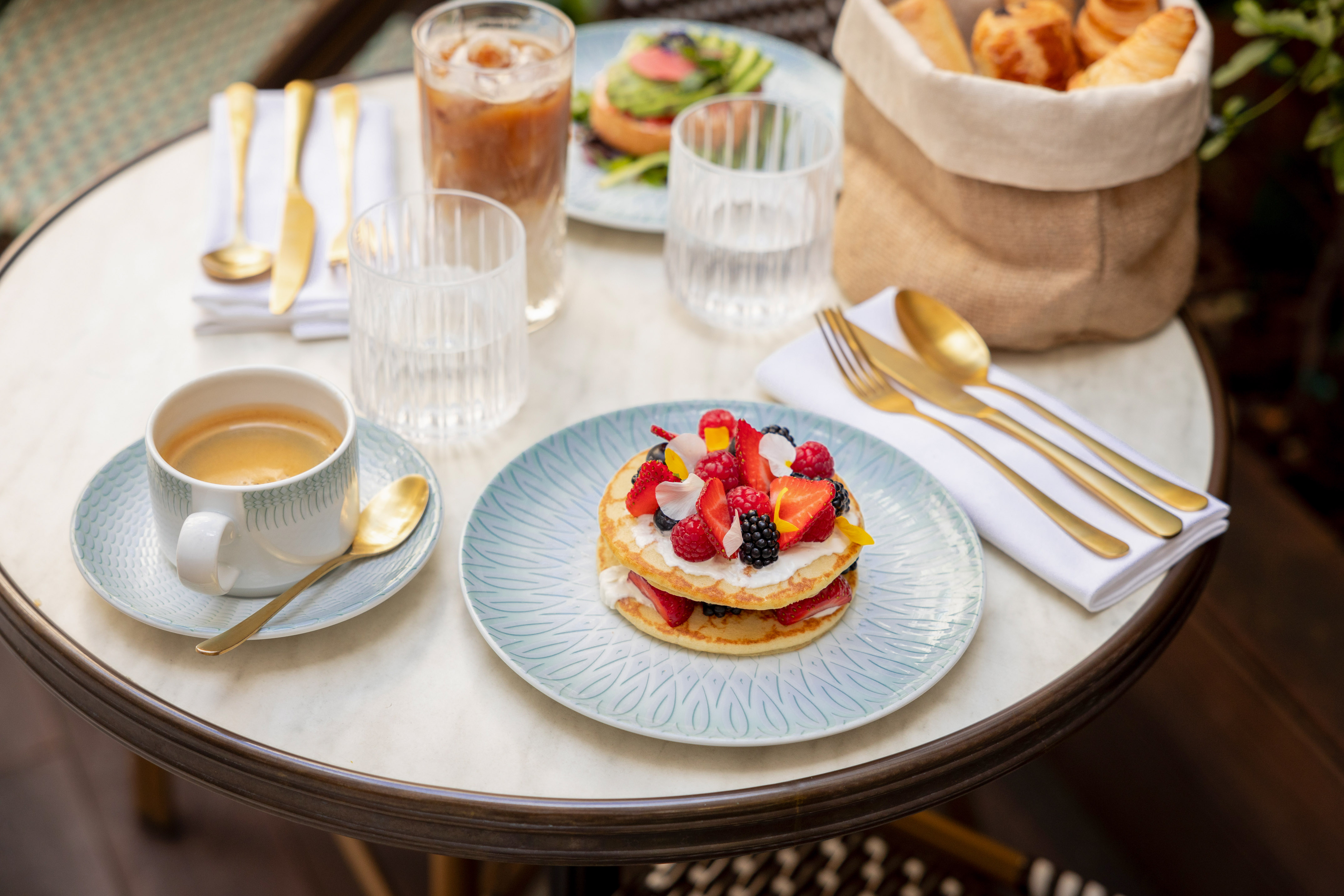 Desayuno en mesa de mármol: tortitas con frutos rojos, café y bollería.