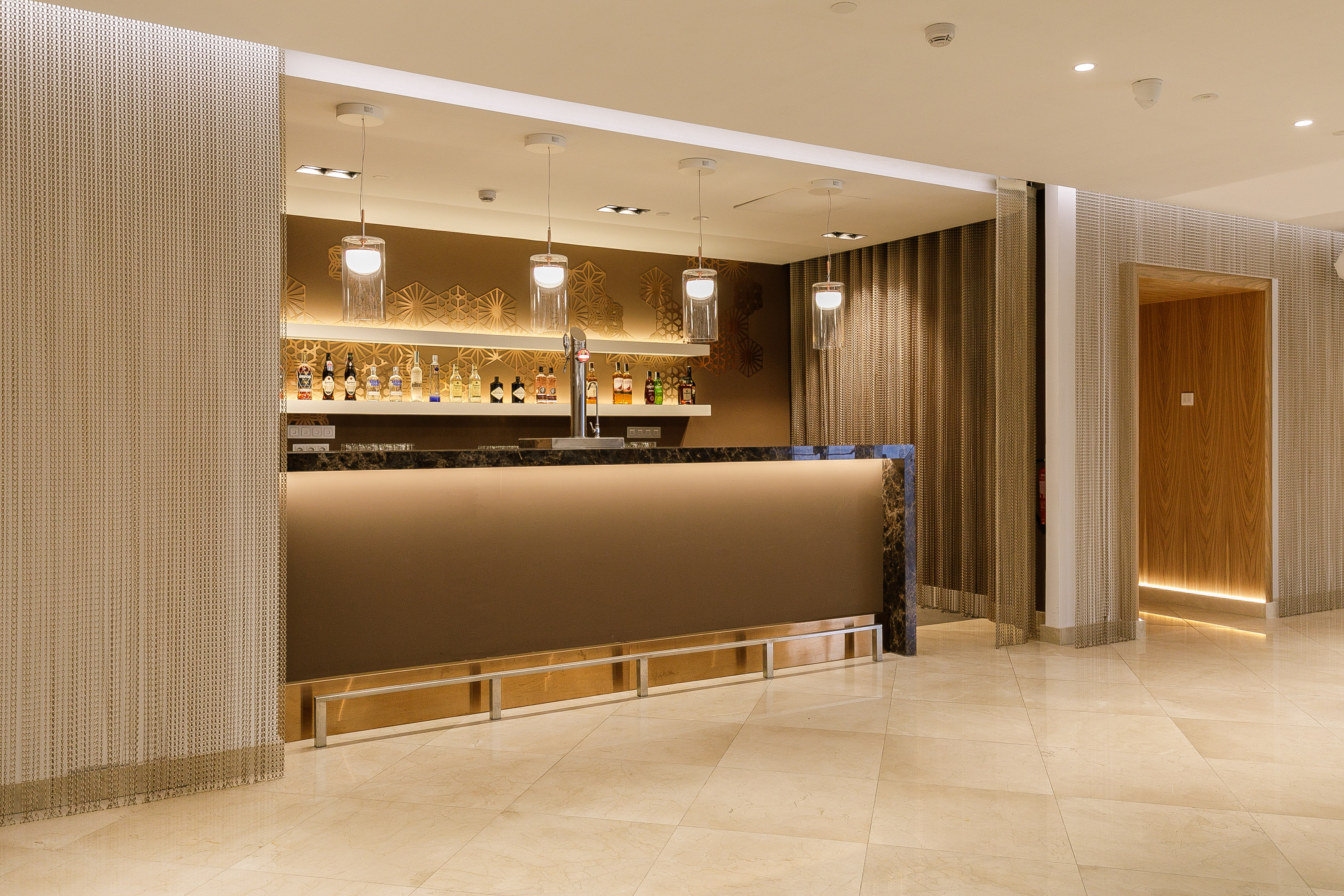 Modern hotel lobby bar with lit counter, liquor bottles, and pendant lights.