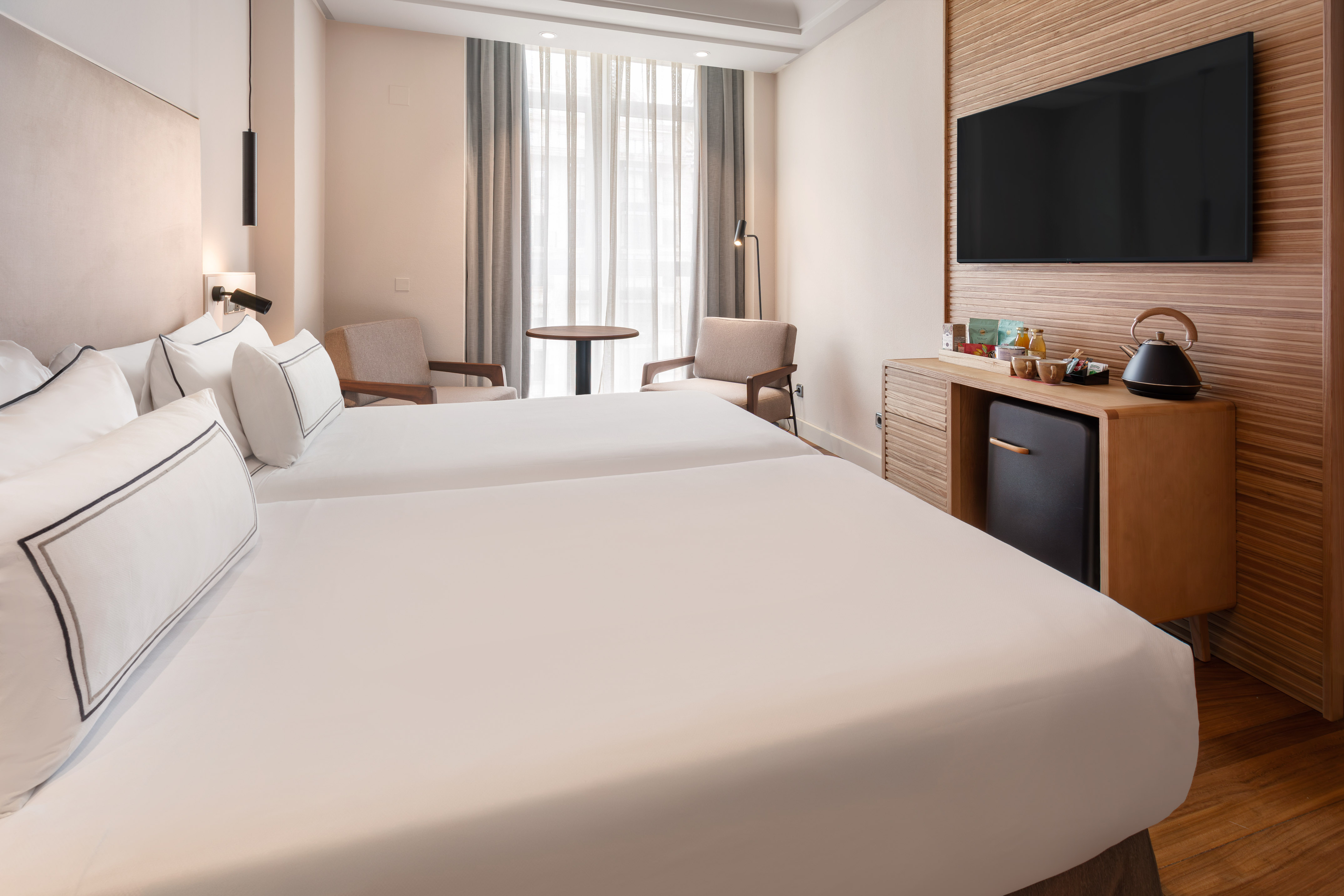 Modern hotel twin guest room with TV, mini-fridge, and comfortable seating area.