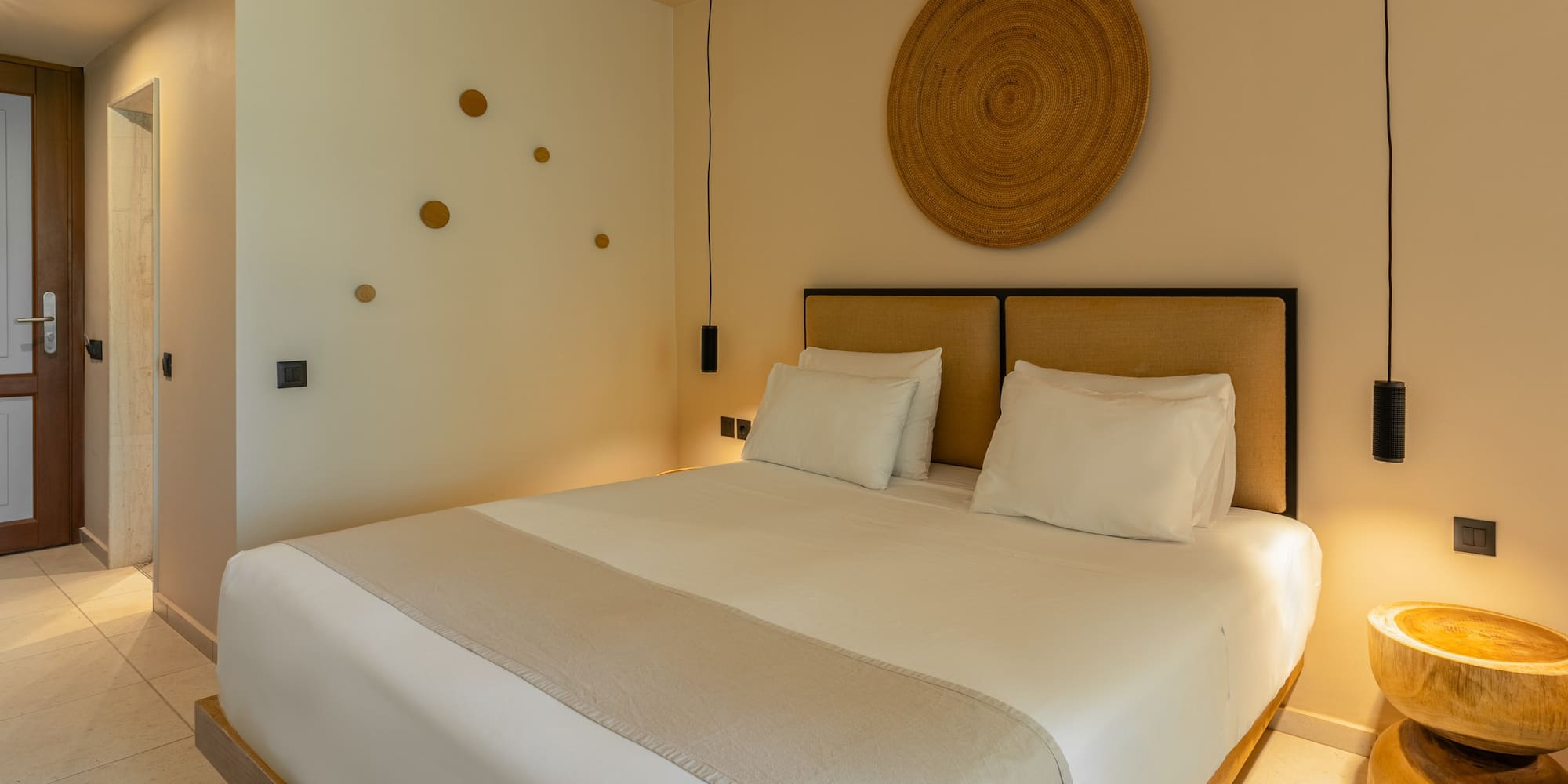 Stylish hotel bedroom with king bed, woven decor, and pendant lights.