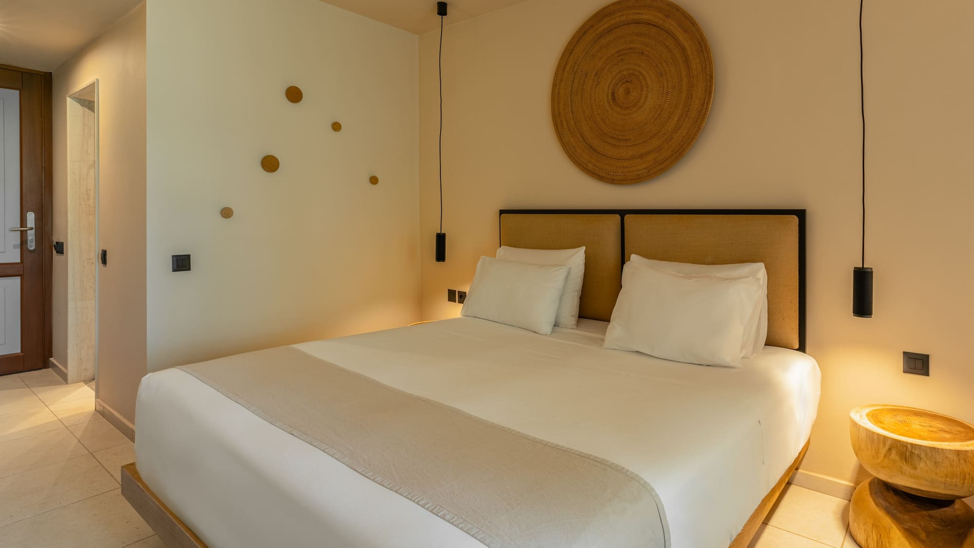 Stylish hotel bedroom with king bed, woven decor, and pendant lights.