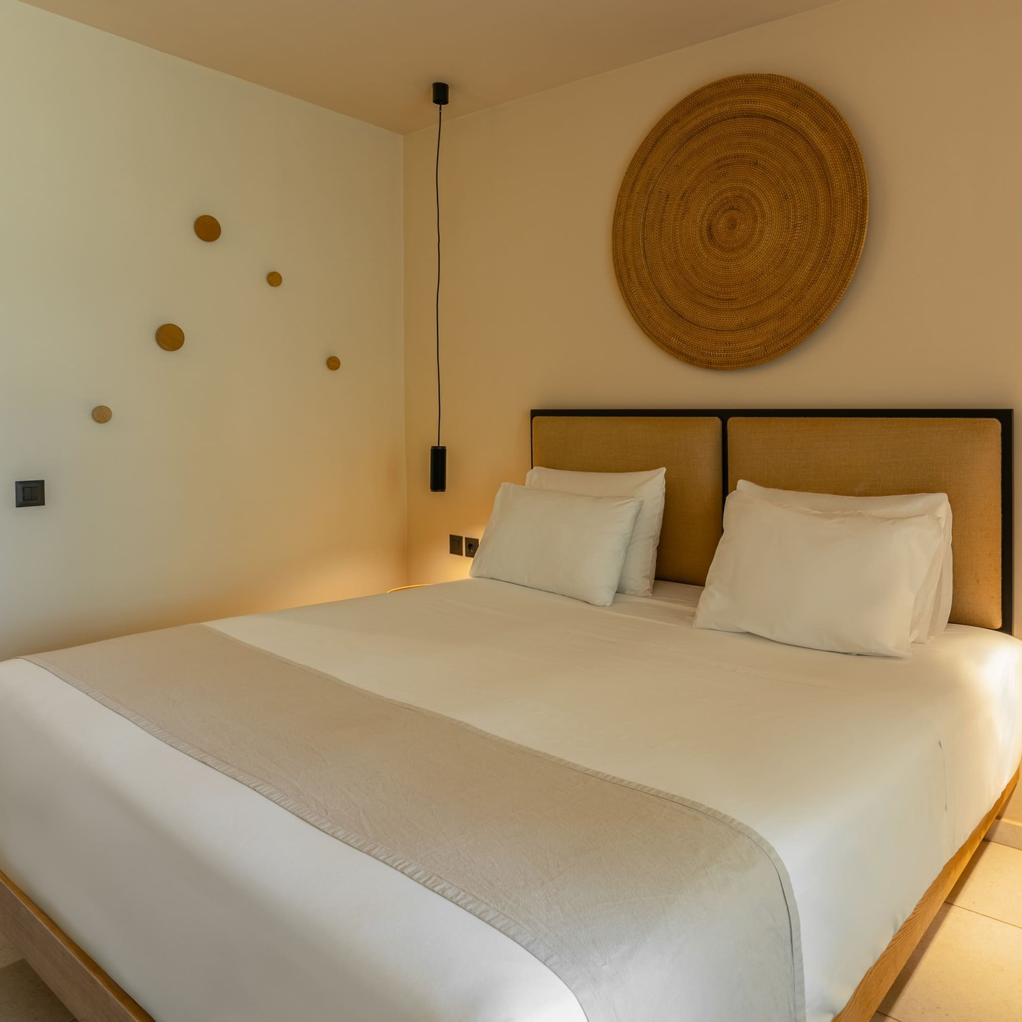 Stylish hotel bedroom with king bed, woven decor, and pendant lights.
