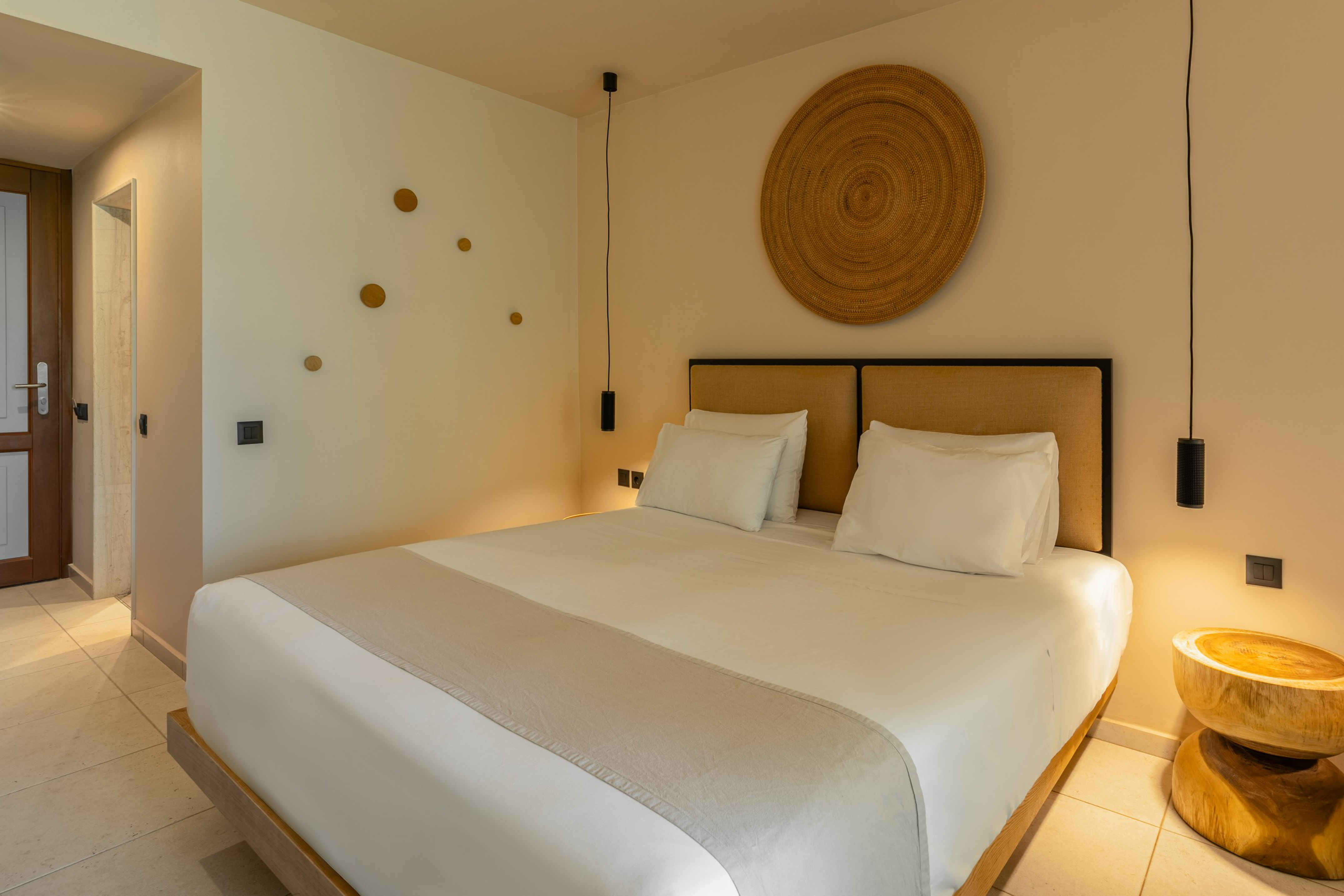 Stylish hotel bedroom with king bed, woven decor, and pendant lights.