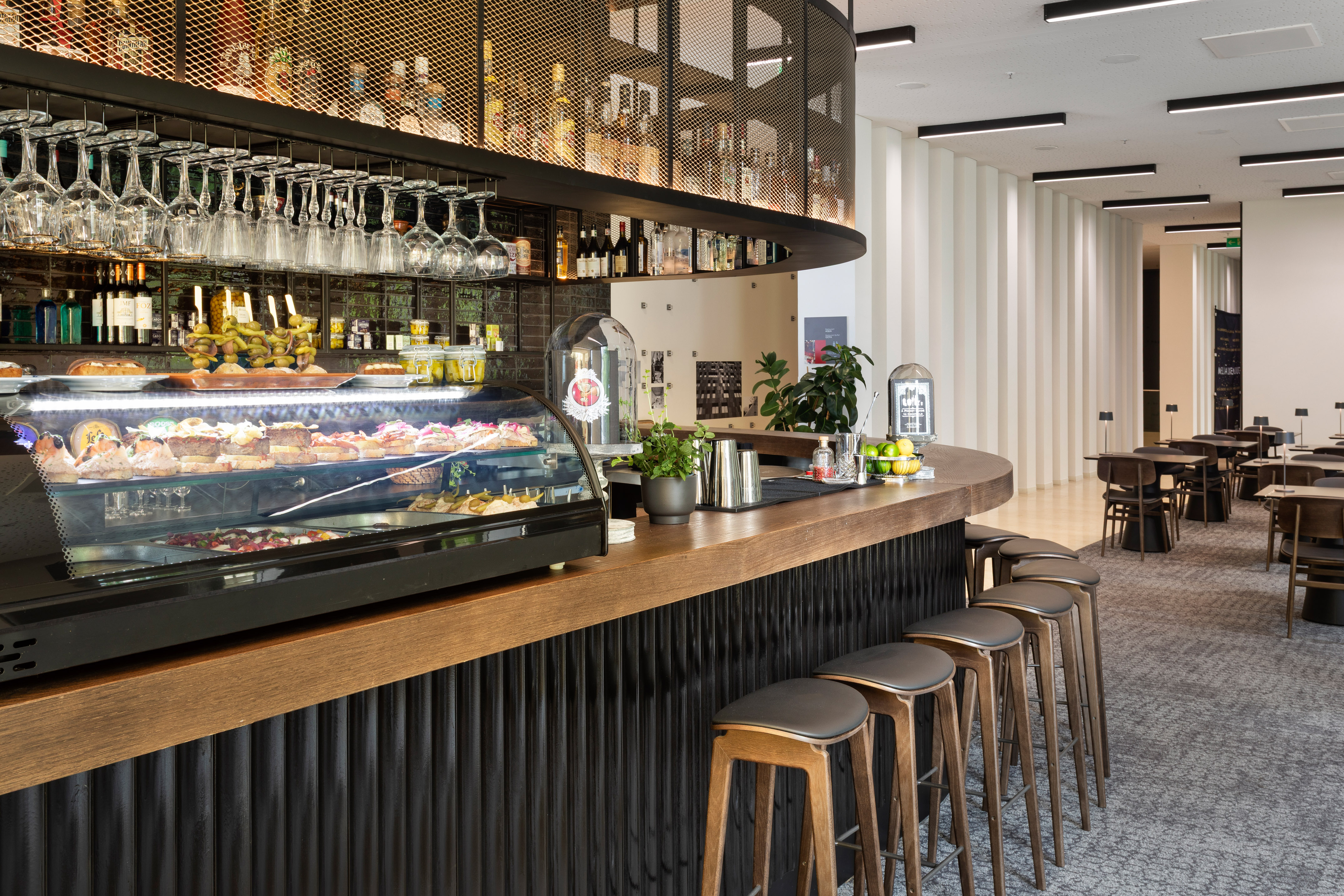 Modern bar interior with food display, sleek bar stools, and drinks shelving.